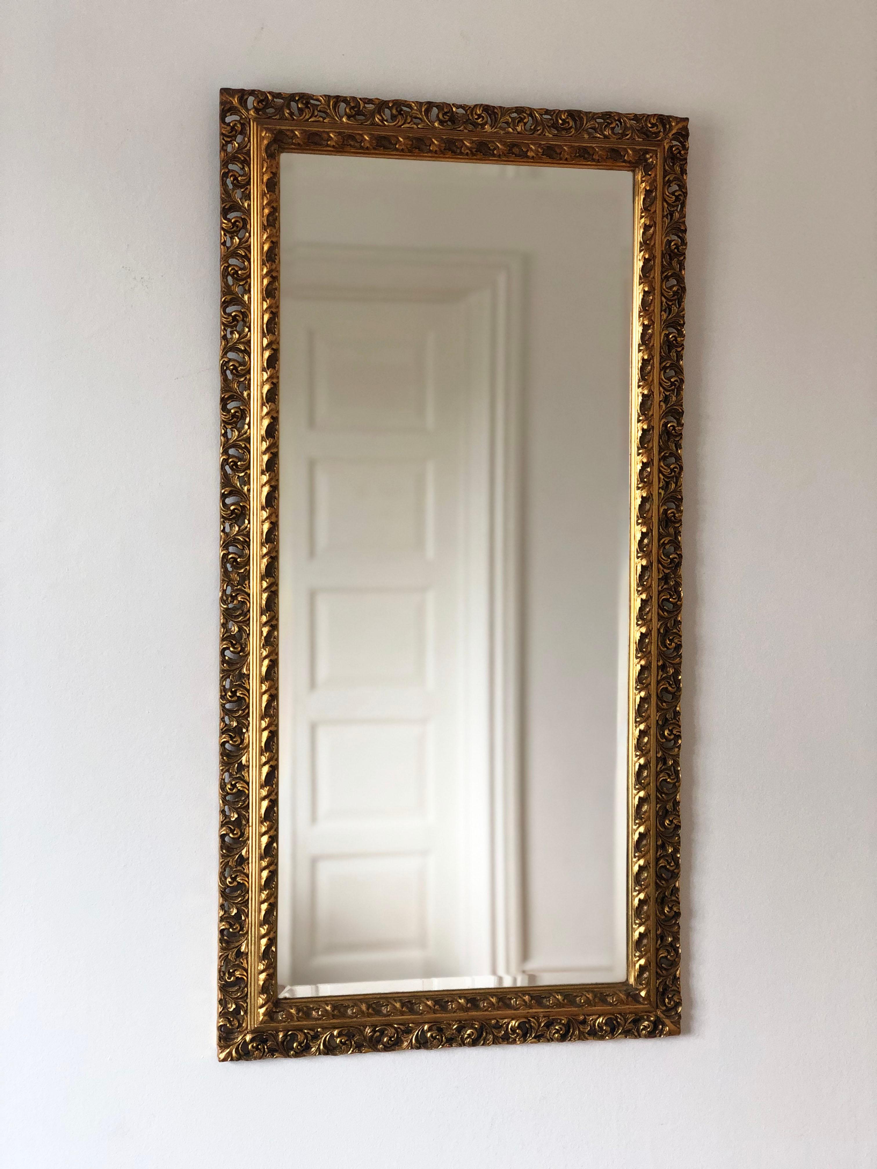 Coppia di specchi da parete vintage provenienti dal Belgio, con cornice in legno dorato intagliata a mano in stile rococò con motivi di volute e foglie traforate. La finitura dorata presenta una leggera patina coerente con l'età. Il vetro smussato