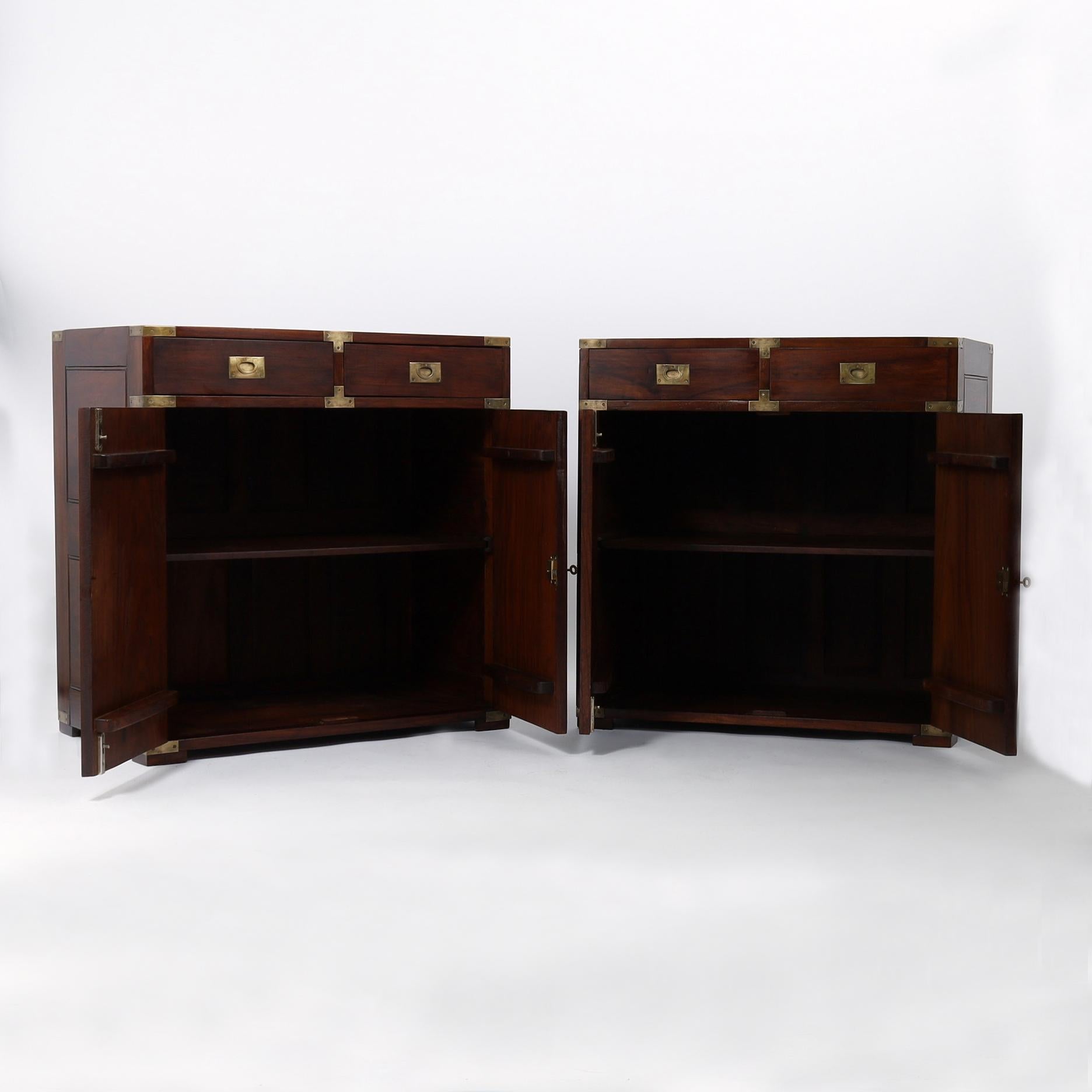 Impressive pair of mid century campaign stands crafted in rosewood featuring paneled sides and tops, campaign brass hardware, two drawers over two doors and block feet. Signed M. Hayat and Bros. in a drawer. 