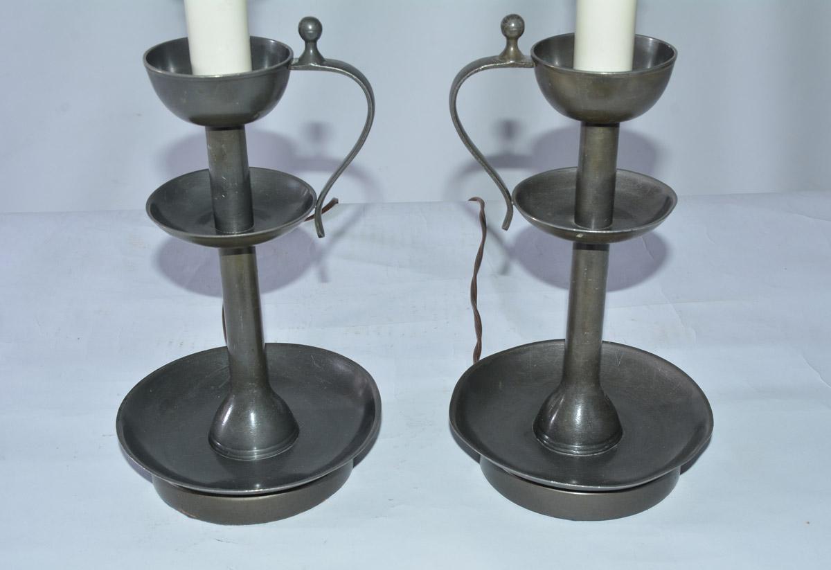 The pair of vintage candleholder lamps are made of pewter and have handles and bobeches. Each lamp holds a single bulb, has a turn switch and is electrified for US use. The brass harps will hold shades.

Measures: Height of lamp with harp 25