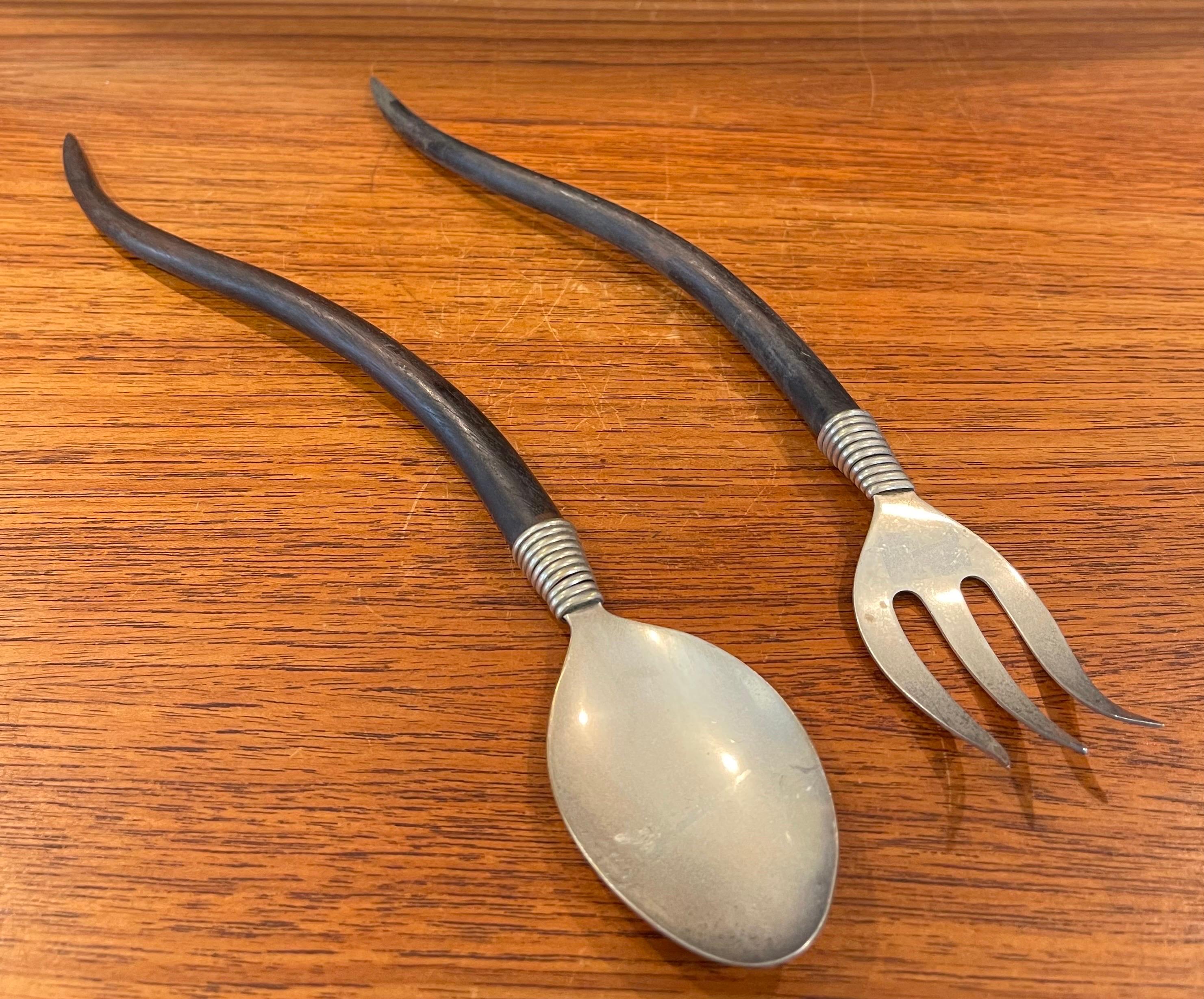 Simple and elegant stylized set of salad servers made of stainless steel and curved wood handles, circa 1960s. The set is in very good vintage condition and measures 12
