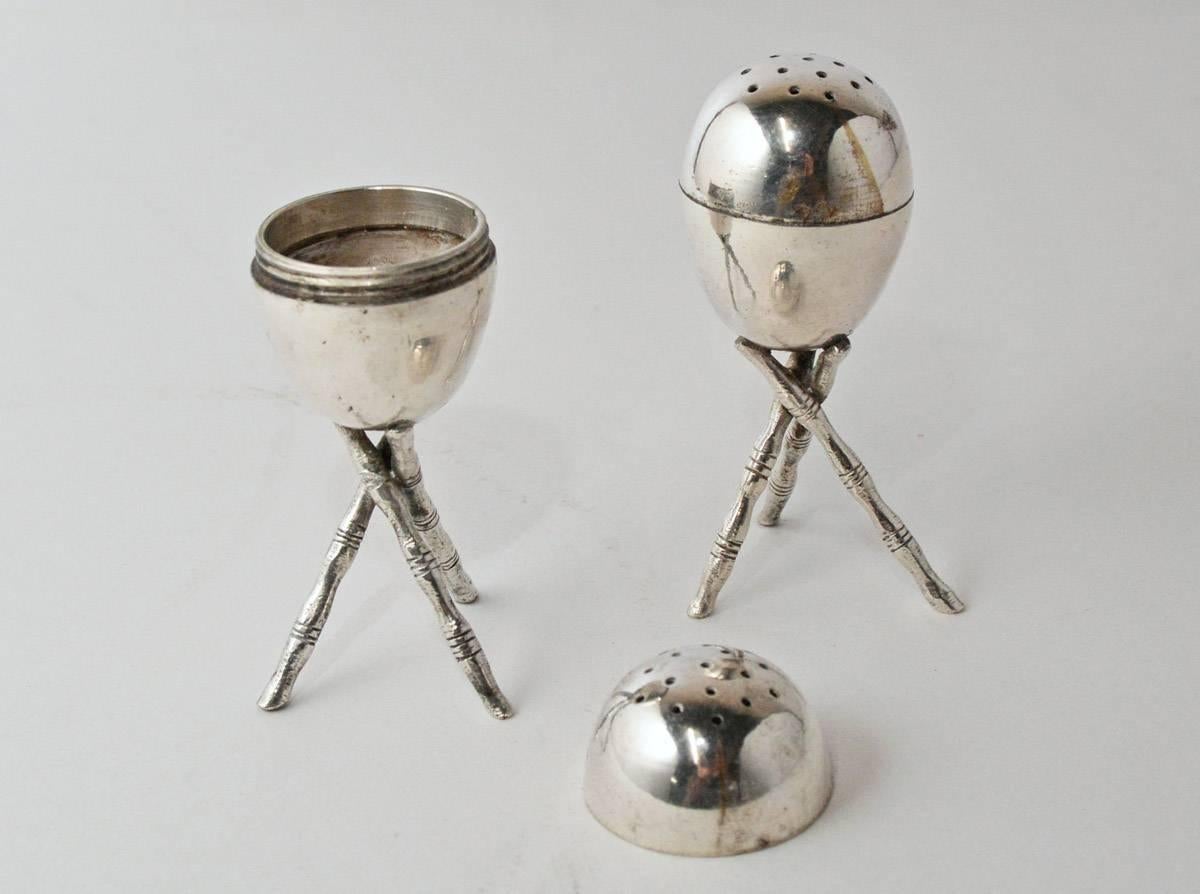 The pair of silver plated salt and pepper shakers are egg shaped and sit on tripods. The tops unscrew.