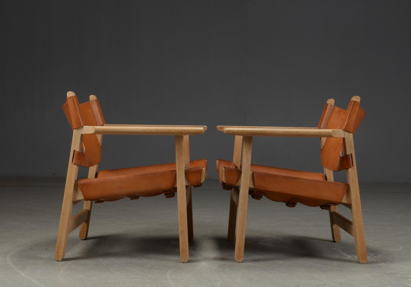 A very good original pair of earlier model Spanish lounge chairs in oak with cognac color saddle leather seats and backs.
 
The earlier models can be distinguished from later versions by the fact they have two cross 'stretchers' at the back rather