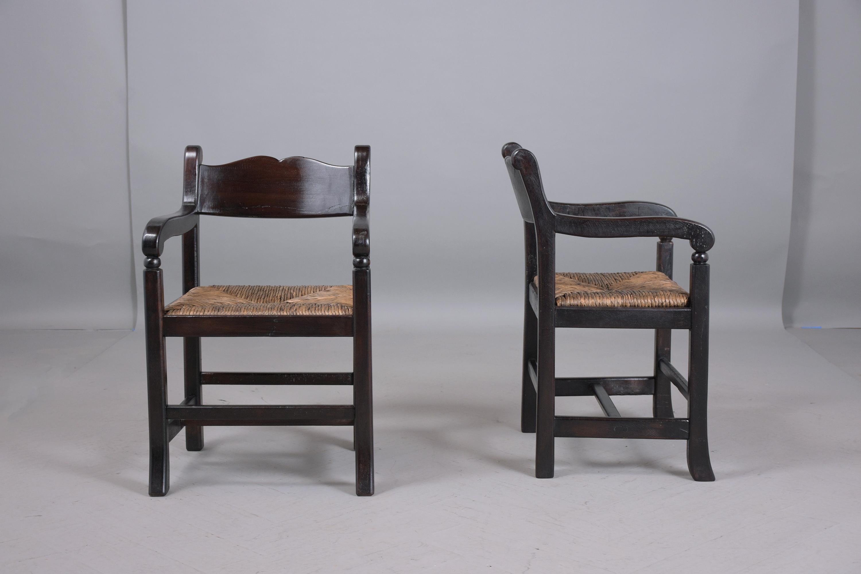 This pair of vintage armchairs are hand-crafted out of teak wood in good condition and features an ebonized color with a beautiful patina finish. The lounge chairs have carved frames with stretched legs and comfortable rush seats. The chairs are