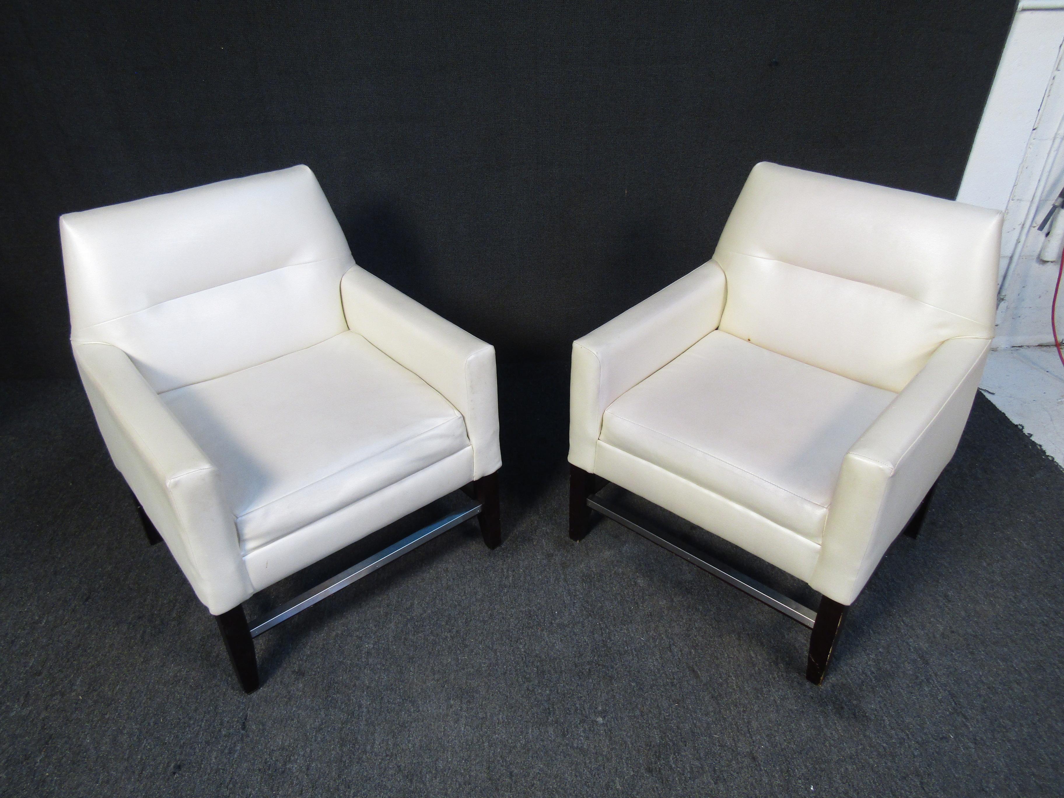 Cette paire de fauteuils club blancs aux lignes pures affiche un style Mid-Century grâce à un design confortable. Le rembourrage en vinyle rend ces chaises faciles à nettoyer et à entretenir. Veuillez confirmer la localisation de l'article auprès du