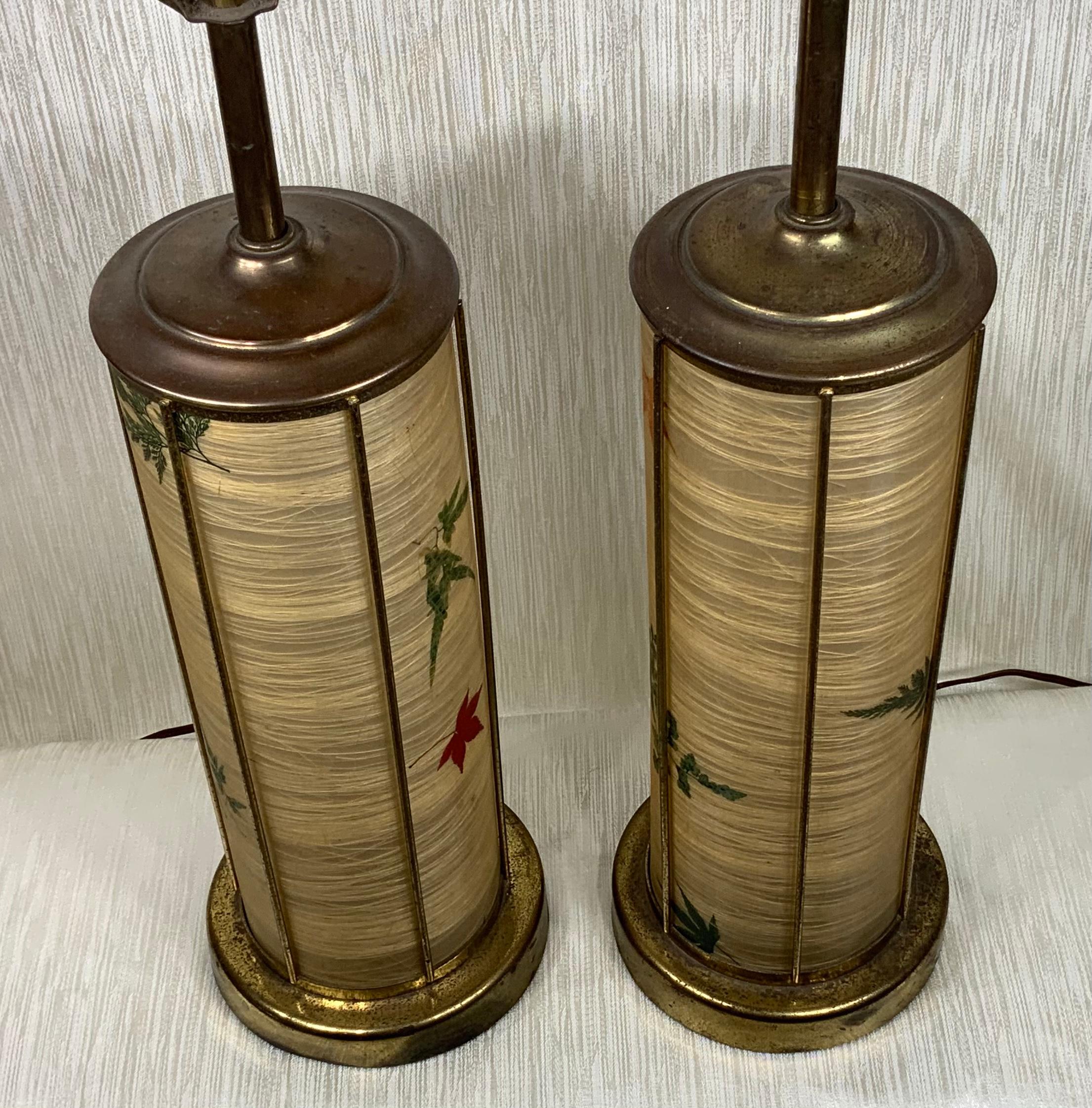 Pair of elegant midcentury table lamps made of brass, with faux parchment shades and base of trees leaves motifs. Included pair of funky lamp finial and three way lighting. Great pair of nostalgic table lamps.