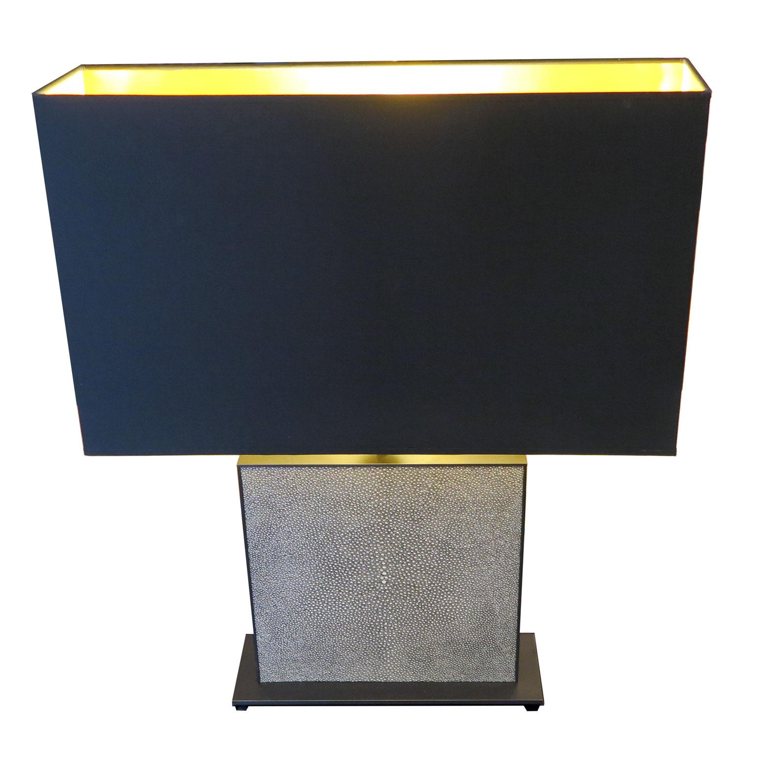 Pair of table lamps with narrow base in brass in oil rubbed bronze coloration. The shades are black and lined with a metallic gold interior emitting a gold light. The shades match the narrow design of the base. Faux embossed shagreen panels line the