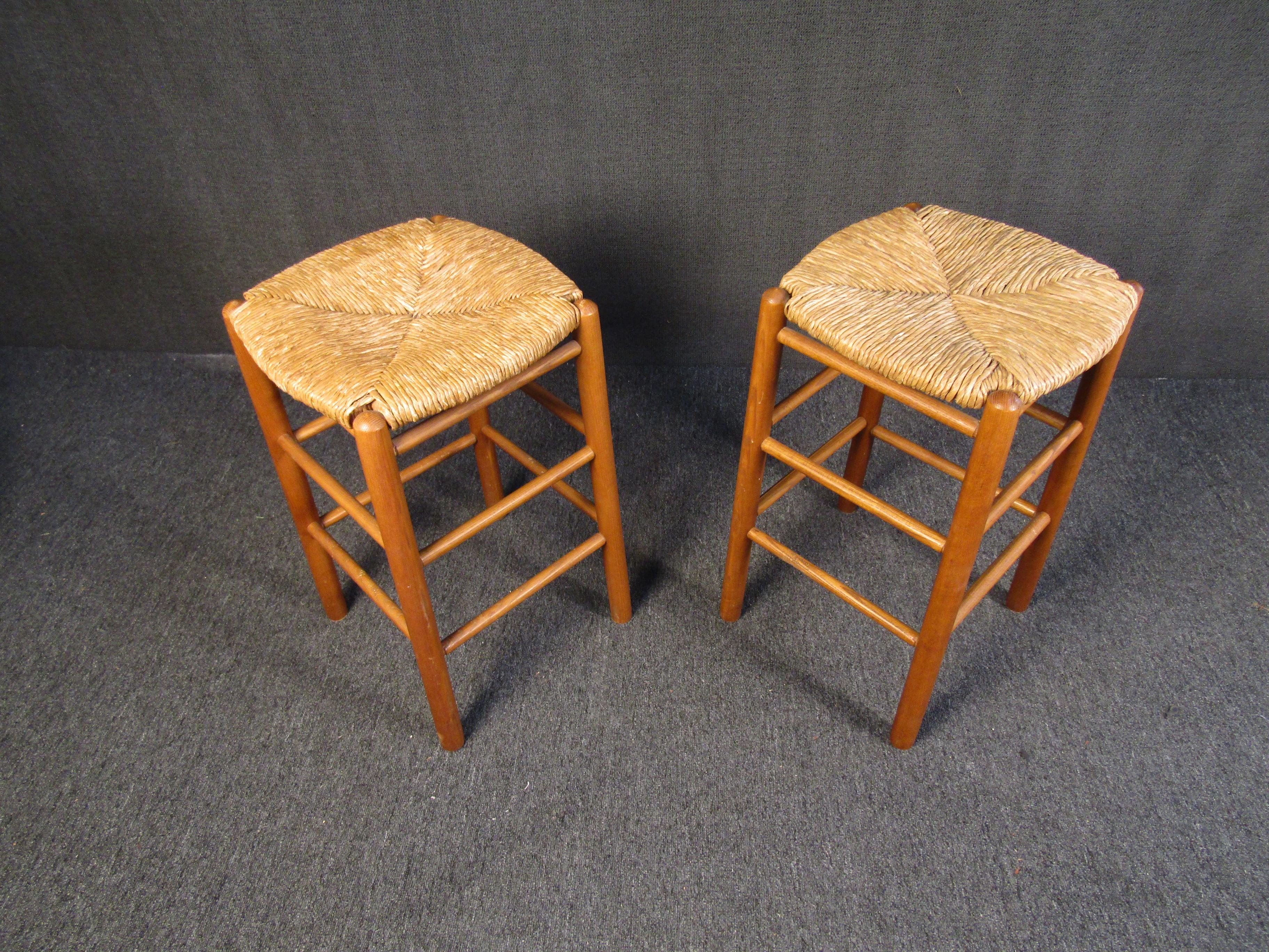 Pair of simple and elegant Mid-Century Modern bar stools combining rich teak frames with woven wicker seats. Please confirm item location with seller (NY/NJ).
