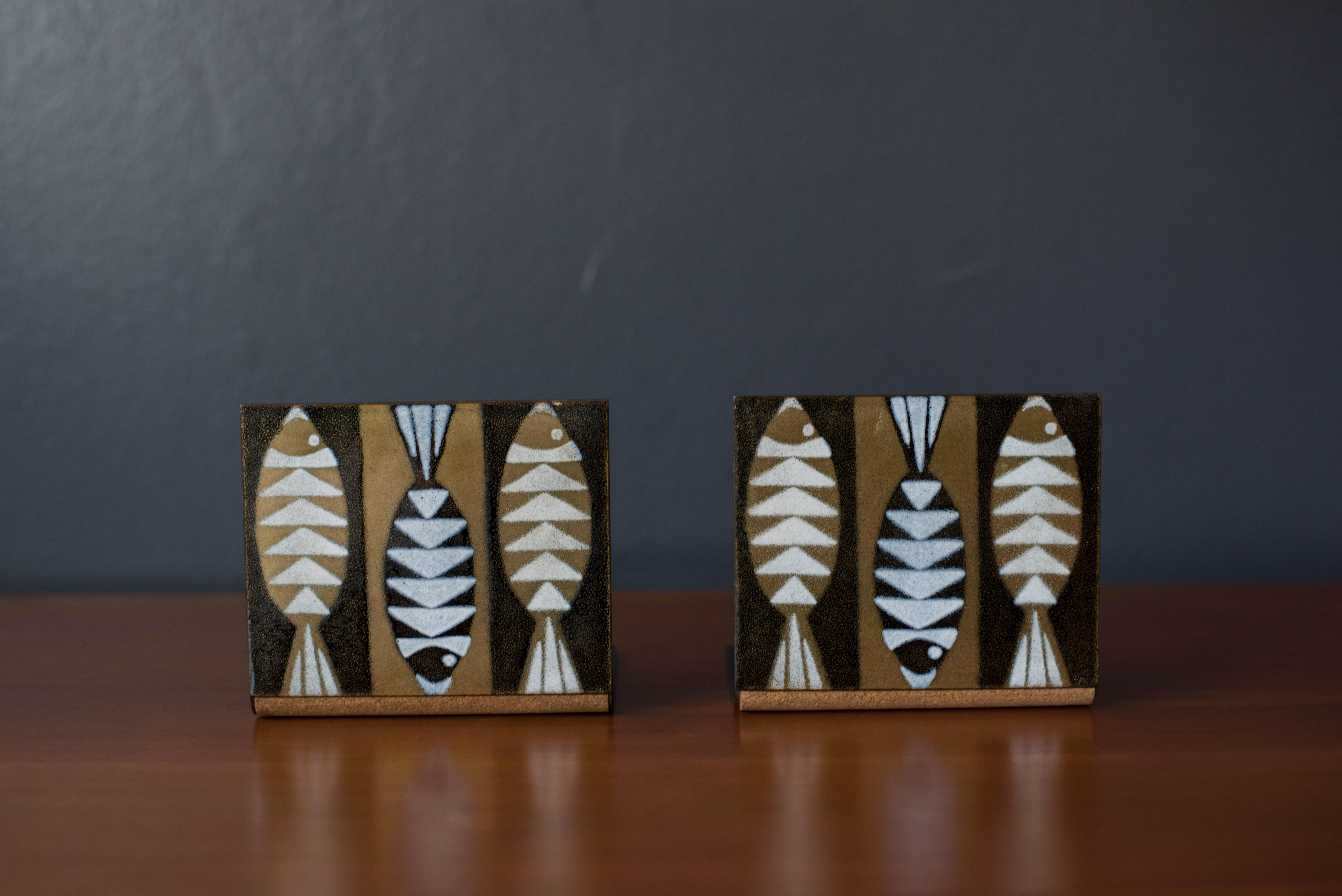 Mid-Century Modern pair of decorative fish bookends designed by Robert Wuersch Associates c. 1960's. This set features contrasting tones of gold, black, and white in a textured metal enamel finish. Equipped with cork bases to protect tabletop