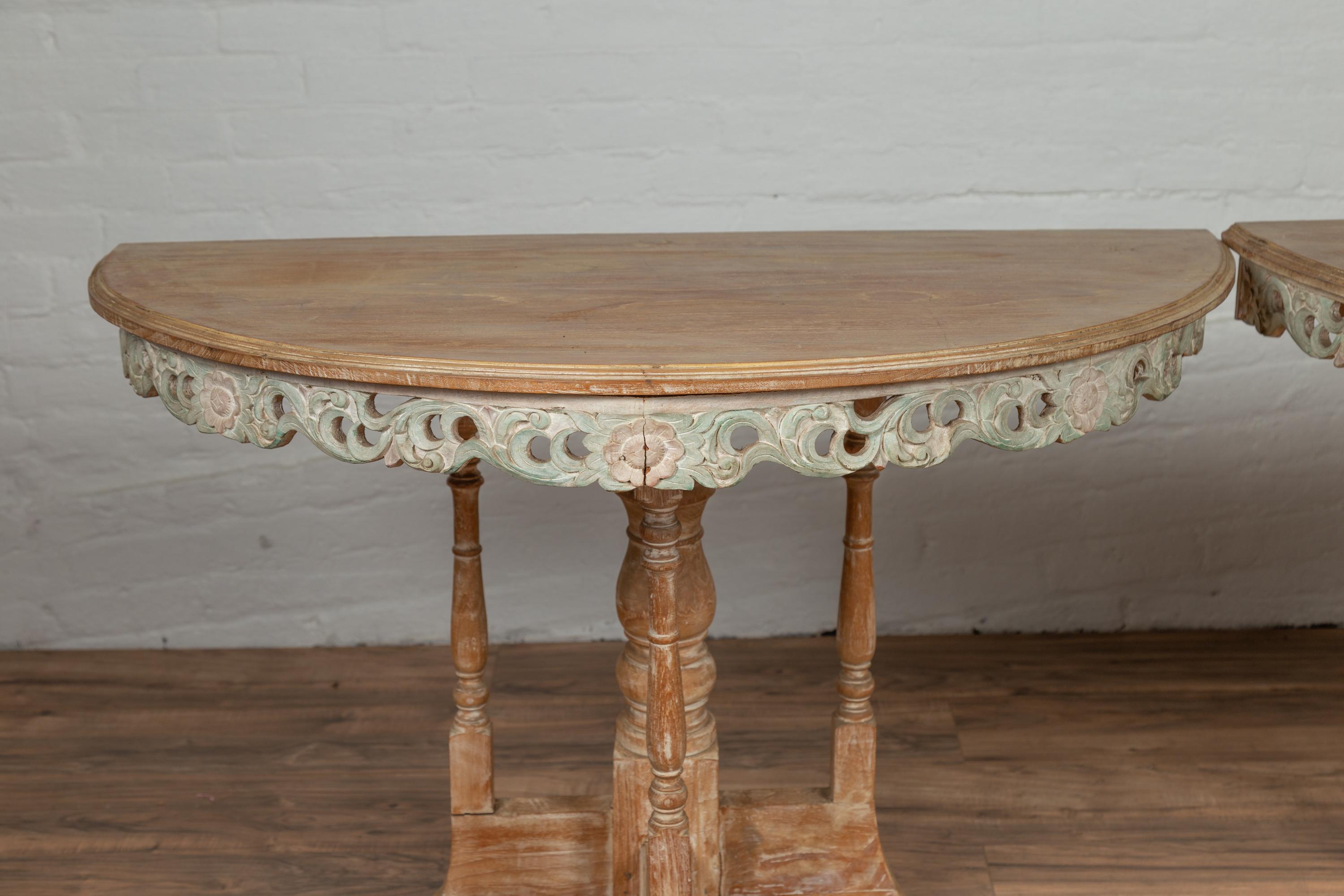 A pair of vintage Thai natural teak demilune console tables from the mid-20th century, with hand carved and painted wooden frieze. Born in Thailand during the midcentury period, each of this pair of demilunes features a semi-circular top with molded