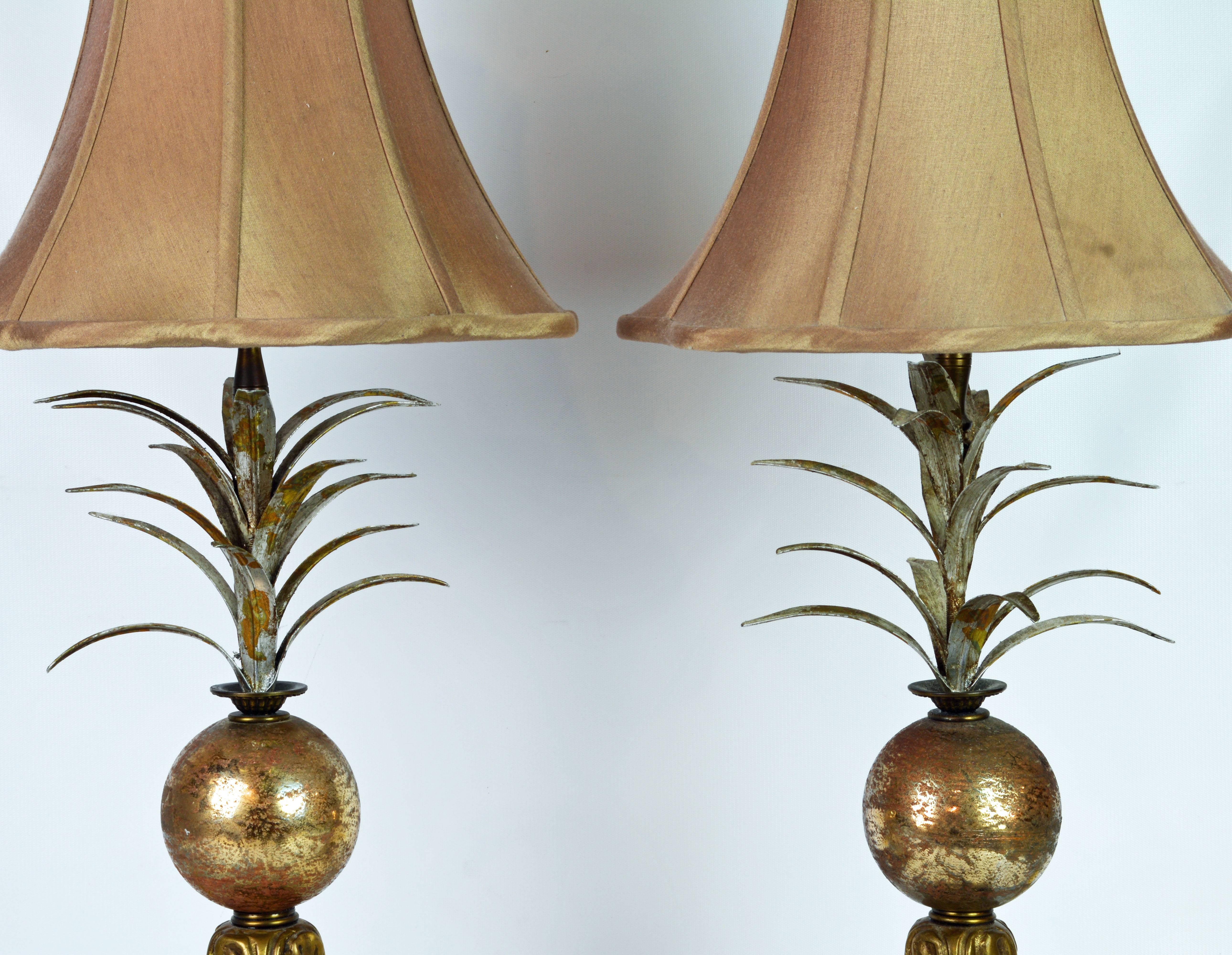 These lamps are early John Richard lamps featuring original shades above a gilt globe holding a frond of likely pineapple leaves and resting on bronze feet standing on bases made of Lucite and distressed giltwood.