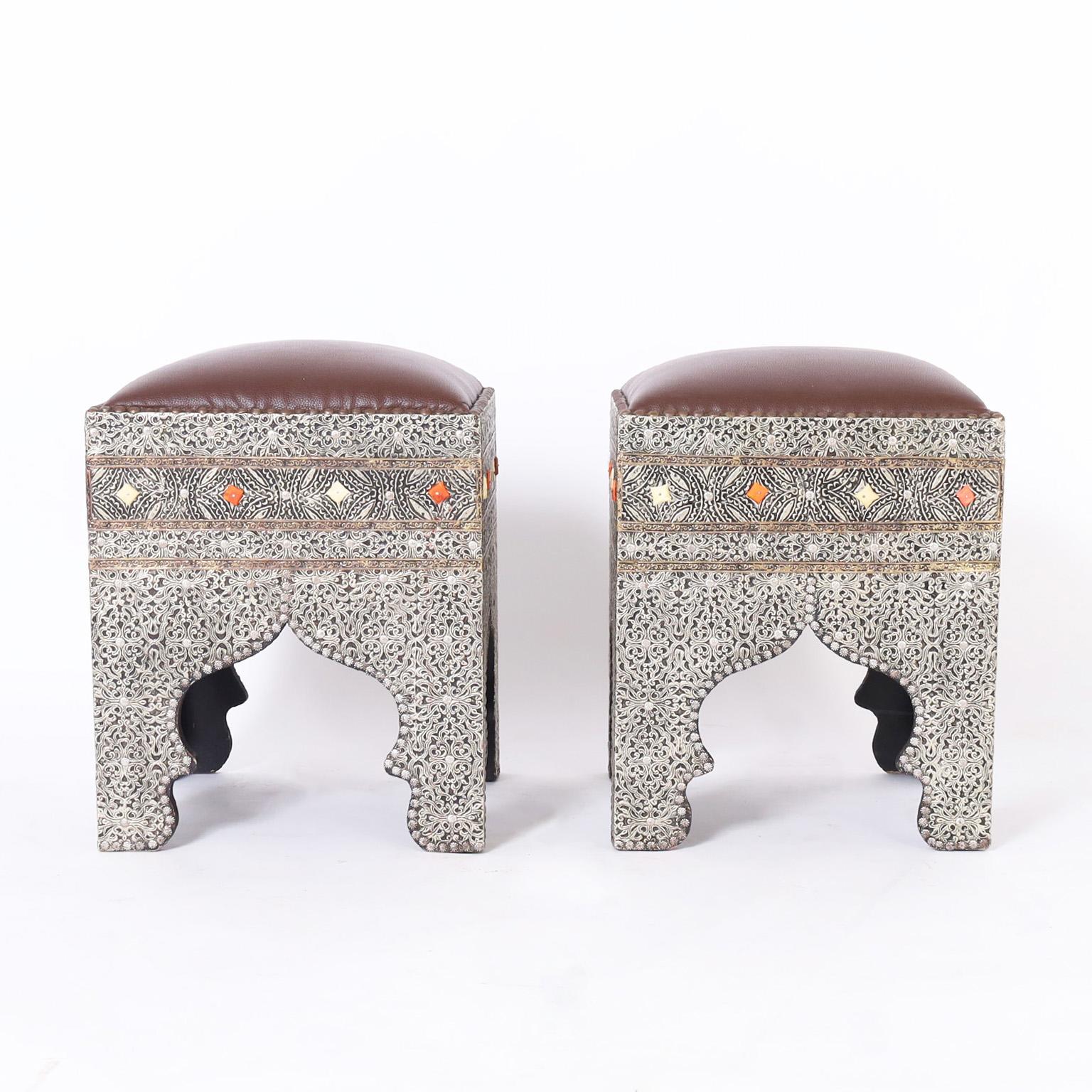 Impressive pair of midcentury Turkish ottomans or stools with upholstered tops with brass tacks over bases having exotic floral metal work, on wood frames, decorated with bone, and having architecturally interesting arches.