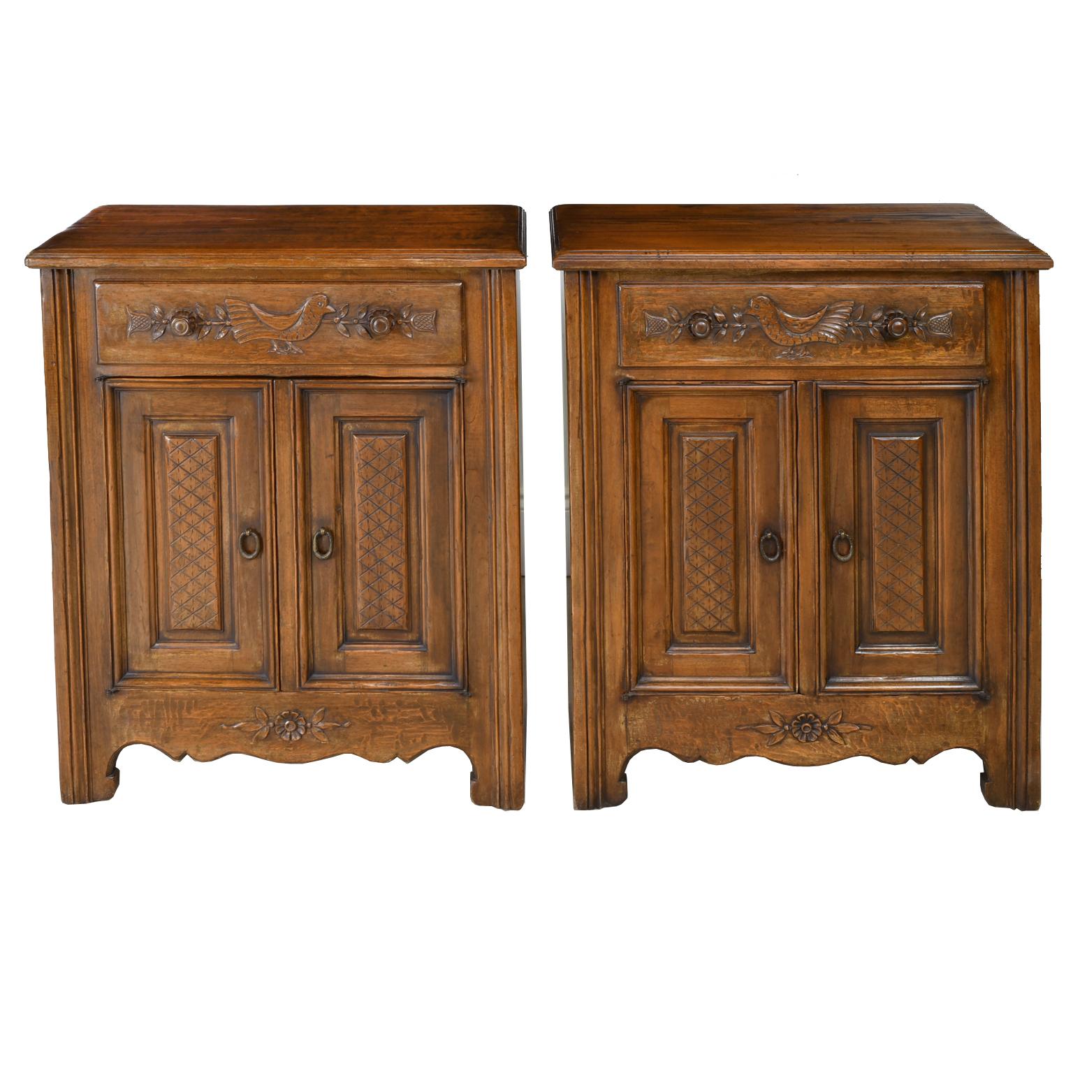 A charming pair of French Provincial style cupboards in walnut with one drawer above two cabinet doors. Carved embellishments include a bird amidst a swag of flowers and foliage on the top drawer, carved lattice design on raised door panels, rosette