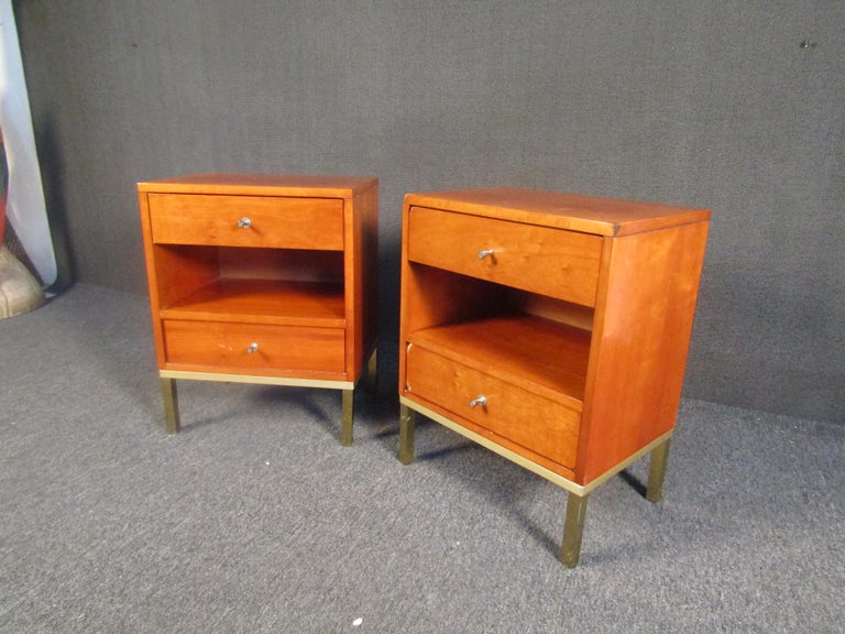 Mid-Century Modern night stands pairing rich walnut with brass, in the style of Paul McCobb. Each night stand contains two drawers and a middle shelf, guaranteeing plenty of storage while adding timeless and versatile Mid-Century style to a bedroom.