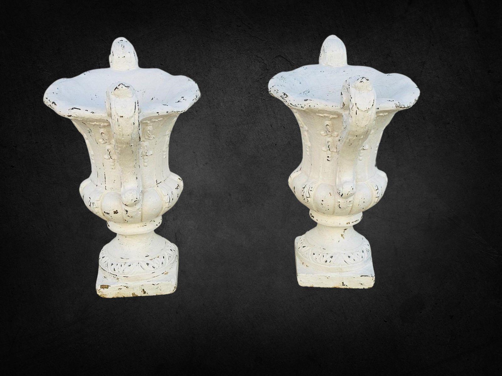 Mejora tu jardín o espacio exterior con este exquisito par de urnas de jardín vintage de hormigón pintadas de blanco. Estas urnas tienen un diseño neoclásico clásico, con asas de elegantes volutas, intrincados detalles en relieve y un elegante borde