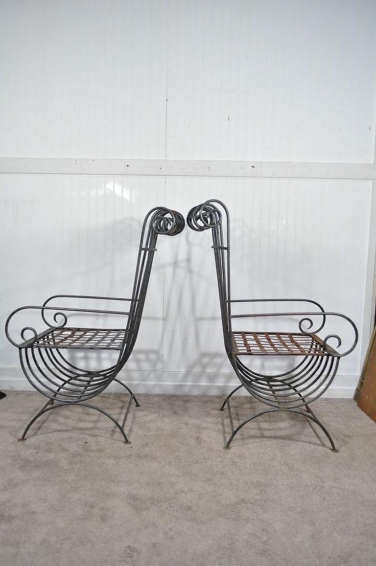 Unique pair of vintage curule base X-form wrought iron armchairs with ornate scrolling backs and arms. These would look amazing with custom decorative pillows, circa mid-20th century. Measurements: 42.75