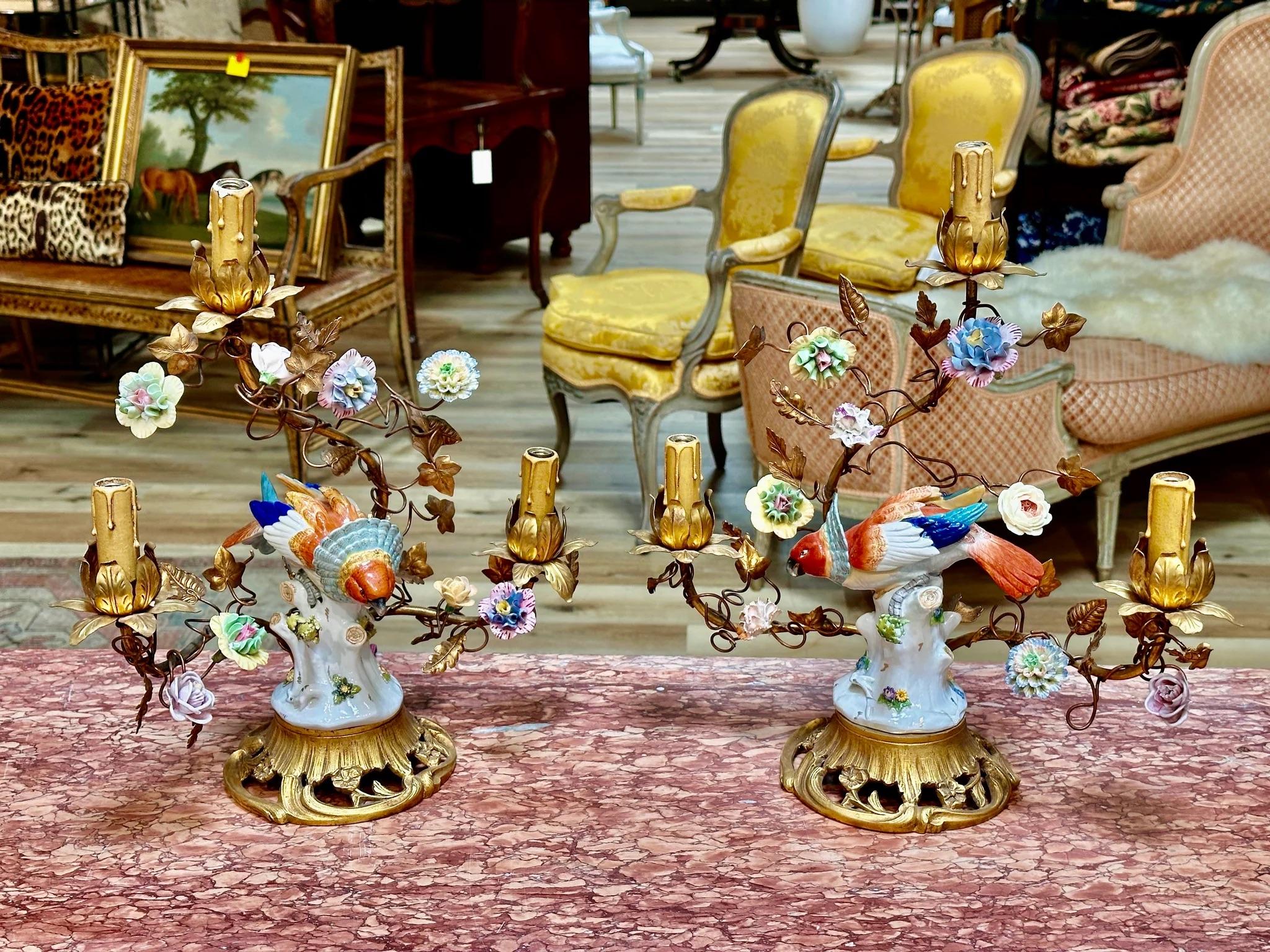Pair of Volkstedt porcelain fan head parrots mounted on French gilt table lamps, Foliate gilt metal three-branch table lamps with applied floral porcelain sprays..  17.5”  h. x 16” w. x 6” d. ).  Wiring newly restored   Volkstedt mark to macaws, c.