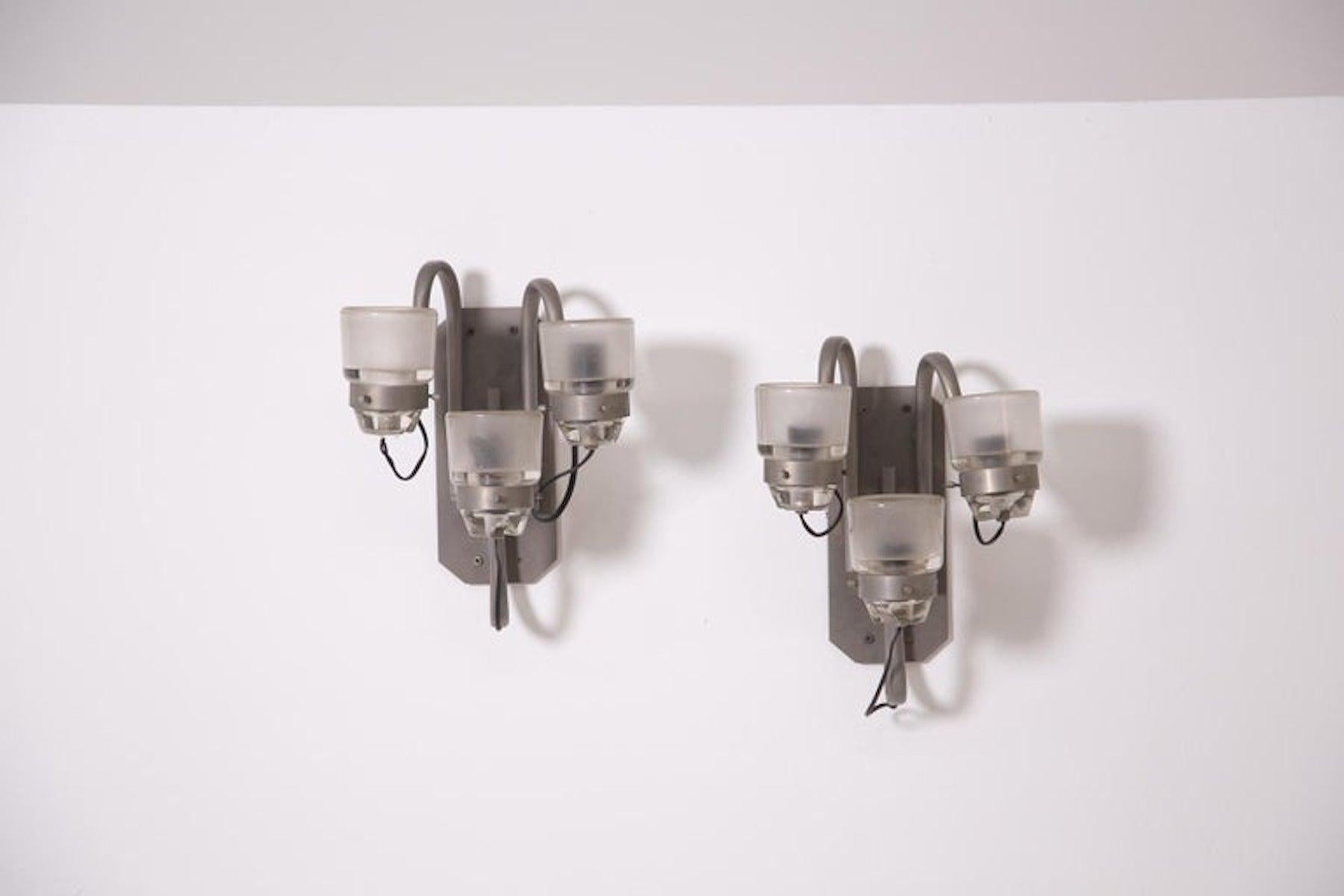 Modern Italian wall lamps designed attr. to Joe Colombo for the OLuce factory.
Each wall lamp has three lights. Its structure is in nickel-plated brass with three arms. At the end of each arm we find its lamp holder in iridescent and frosted glass