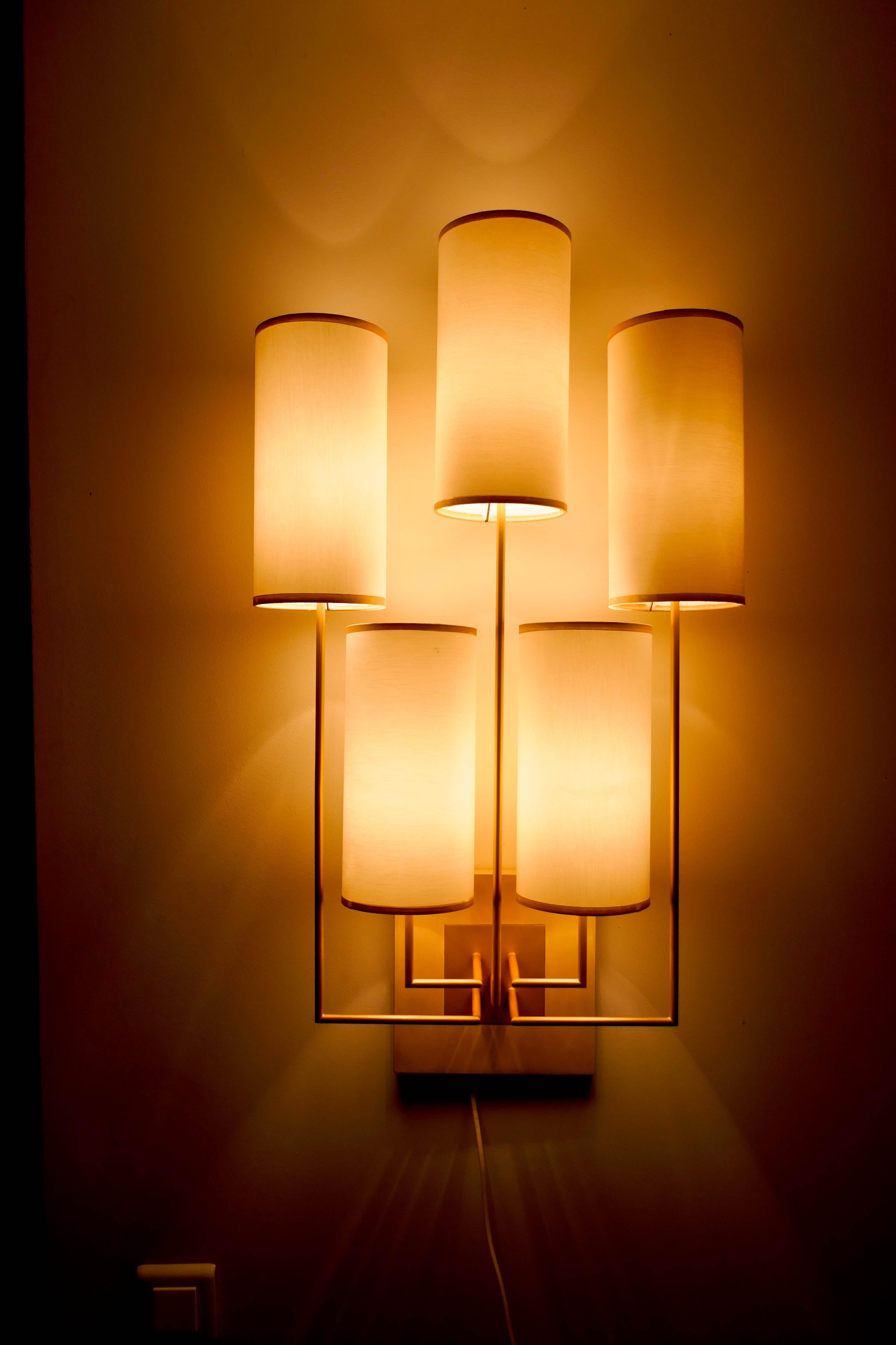 Ein Paar Wandleuchten aus Metall mit goldener Patina, die Sockel sind aus Kastanienholz. Die Lampenschirme sind mit weißem Stoff bezogen.
Diese Leuchte ist neu, aber sie wurde für eine Ausstellung verwendet.