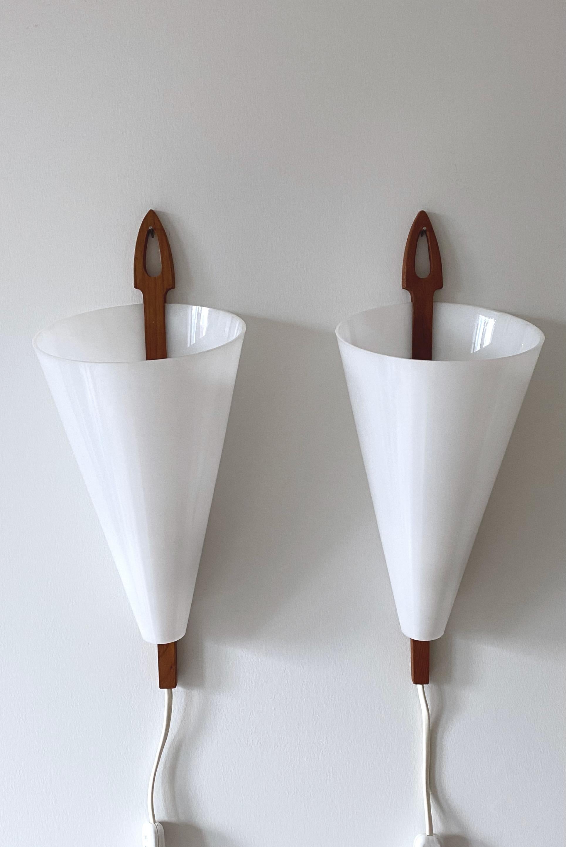Pair of Wall lamps by iconic Swedish Mid-Century lamp designer Hans-Agne Jakobsson for him eponyms brand in Markaryd, Sweden. Hard plastic white lamp shades with a simple and classic teak arm design. Very good condition with the designers label on