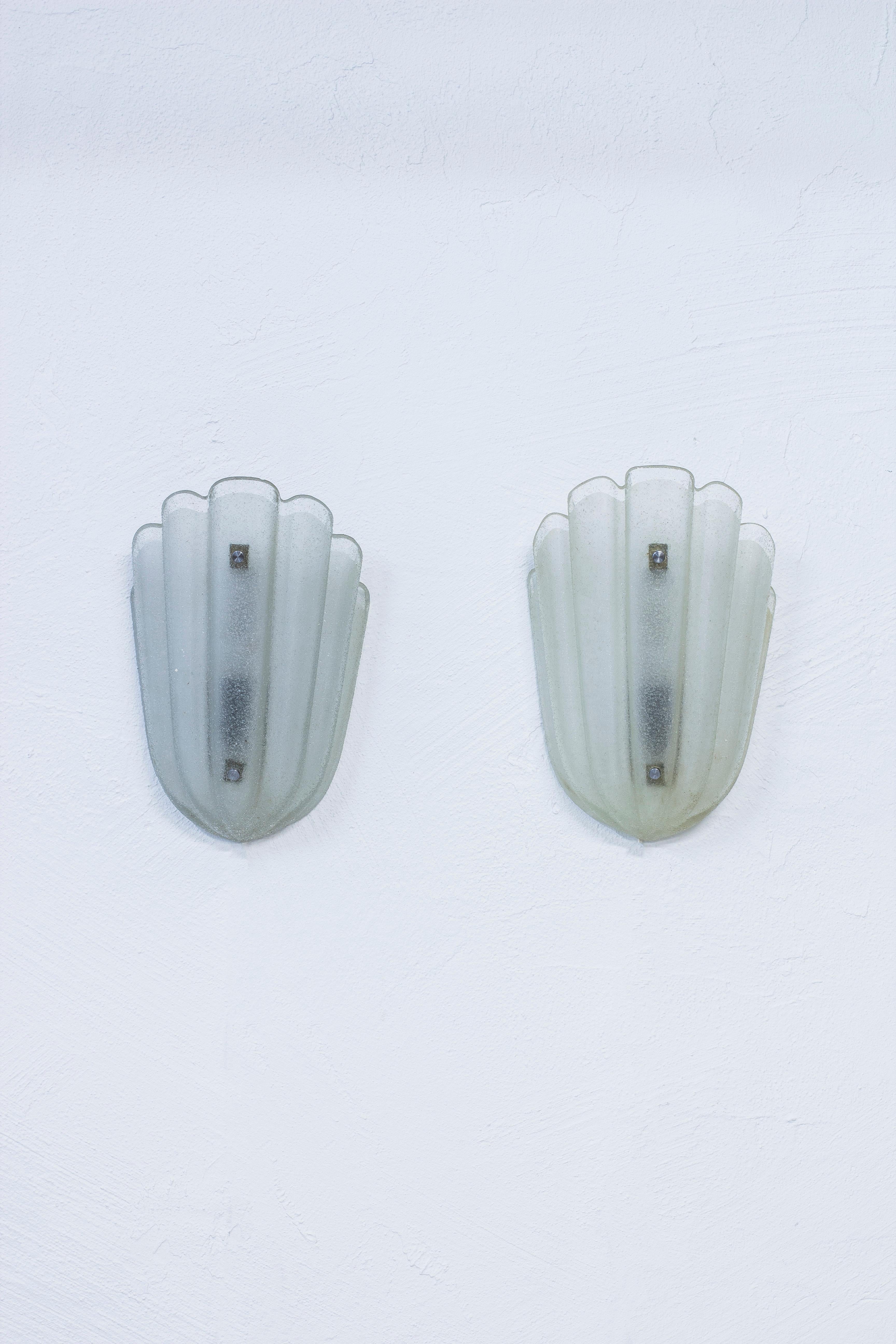 Pair of wall lamps produced in Sweden during the 1940s by Orrefors. Made from clear white glass with a hint of blue. Nickel plated bolt details. In working order with new electric cables. Good vintage condition with age related use and