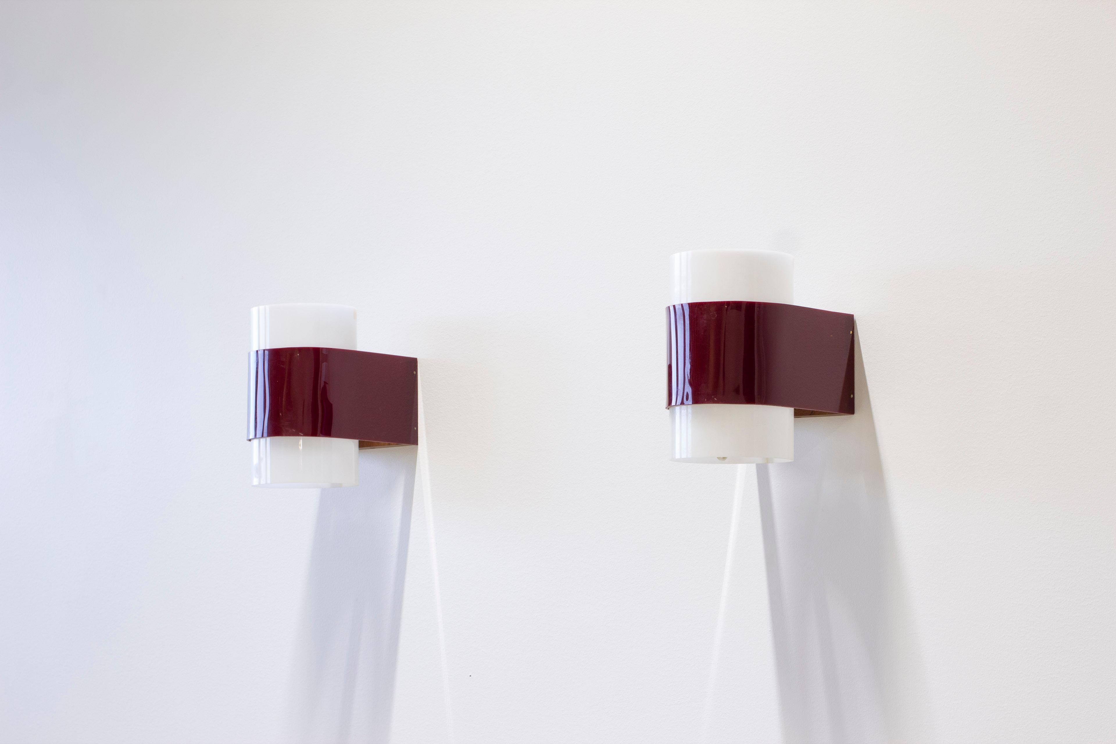 Coppia di lampade da parete disegnate da Yki Nummi. Prodotto in Finlandia da Orno negli anni 1950-60. Realizzato in acrilico rosso e bianco con schienale in teak e dettagli in ottone. Condizioni vintage molto buone con leggera usura e patina dovuta