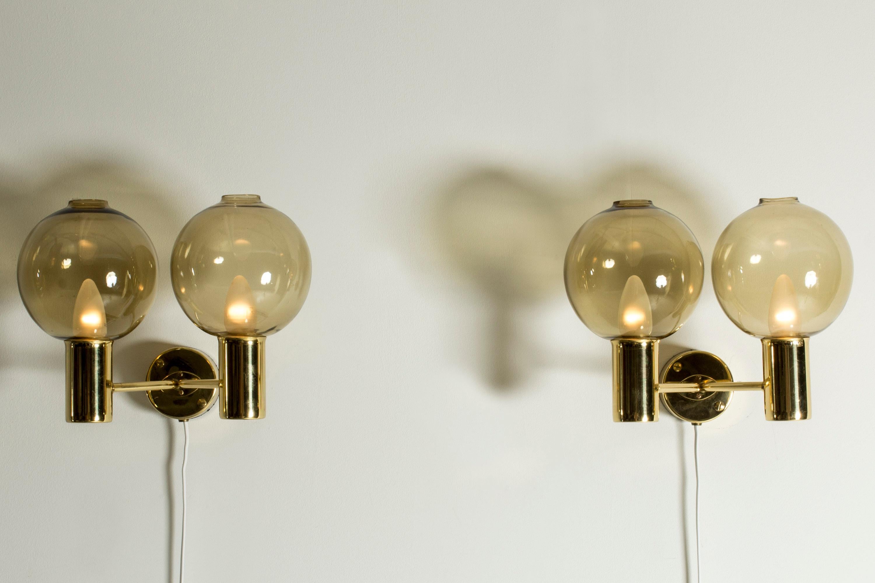 Pair of wall lamps by Hans-Agne Jakobsson, with brass frames and smoke colored glass shades. Sleek brass forms combine with the soap bubbly lightness of the shades.