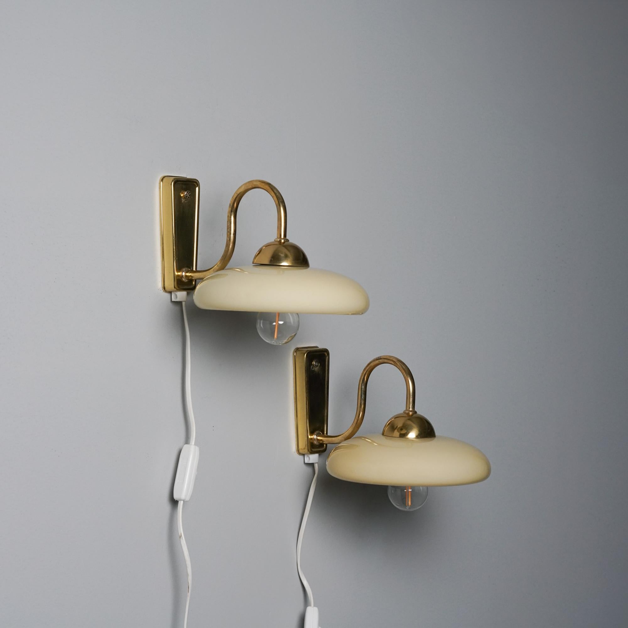 Pair of wall lights, manufactured in Finland, 1970s. Brass frame with opaline glass shades. Good vintage condition, minor patina consistent with age and use. 
 