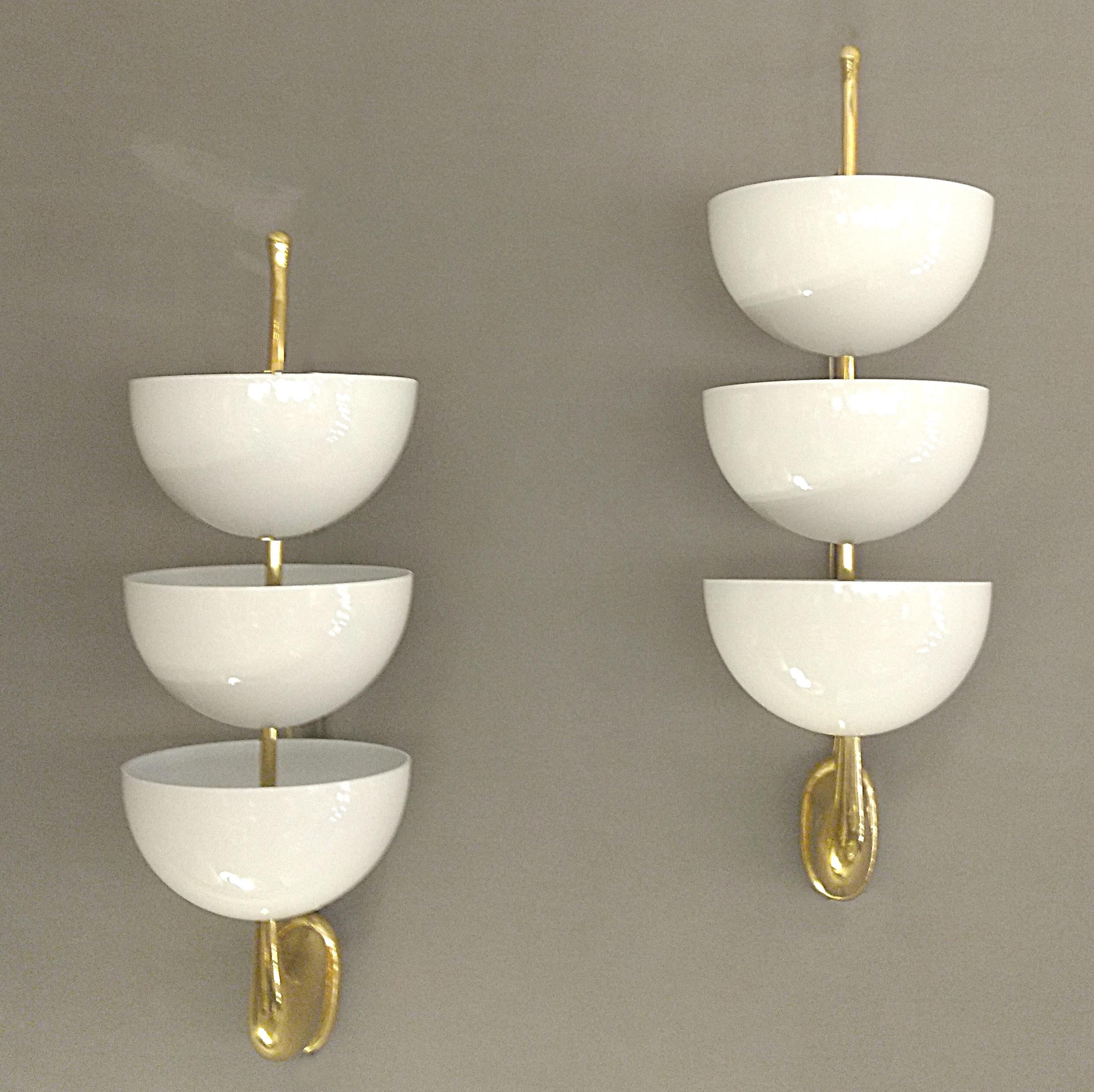 Pair of wall sconces in solid brass and lacquered sheet metal, Italy circa 1960.
Three deep round cups, cream lacquered on the outside and white on the inside, each conceal an electric bulb. They are mounted on an upward-facing brass arm, ending in