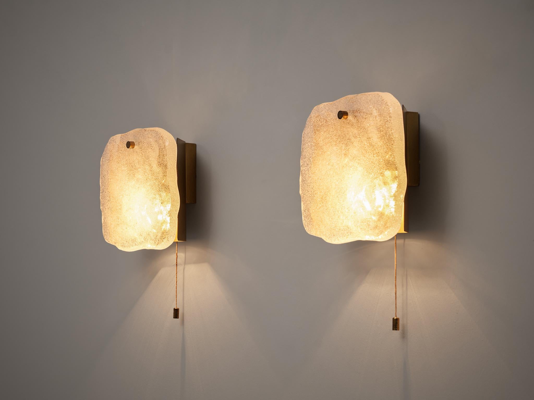 Wall lights, brass, glass, Europe, 1960s

A thick structures glass plate with curved contour hides the light bulb. The glass is fixated to the wall with a polygonal brass element. Due to the thick glass, the light partition is atmospheric, which