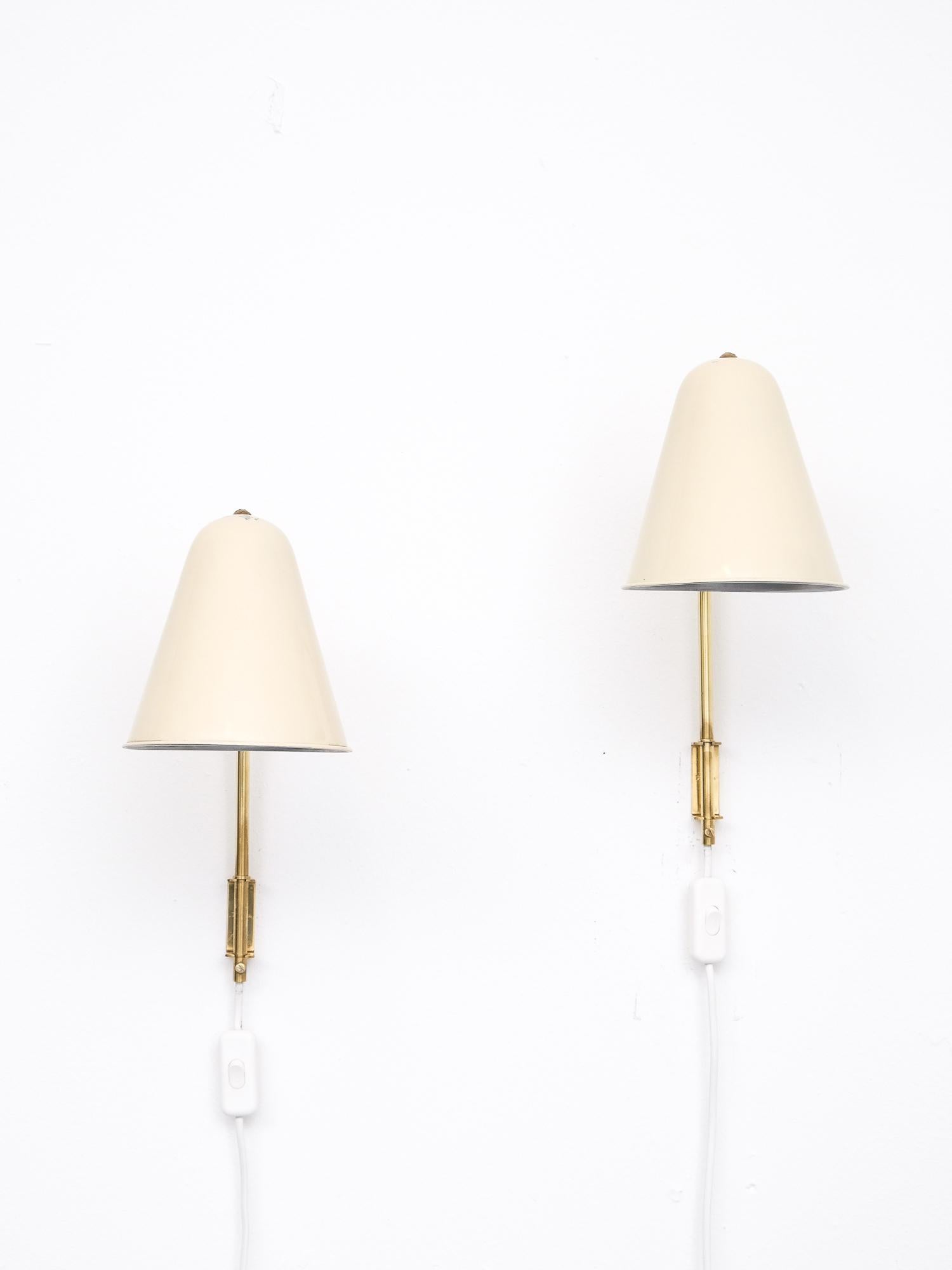 A pair of 1950s solid brass adjustable wall lamps with cream color painted shades. A beautiful and elegant design by Paavo Tynell for Idman Oy. Model number 71030.