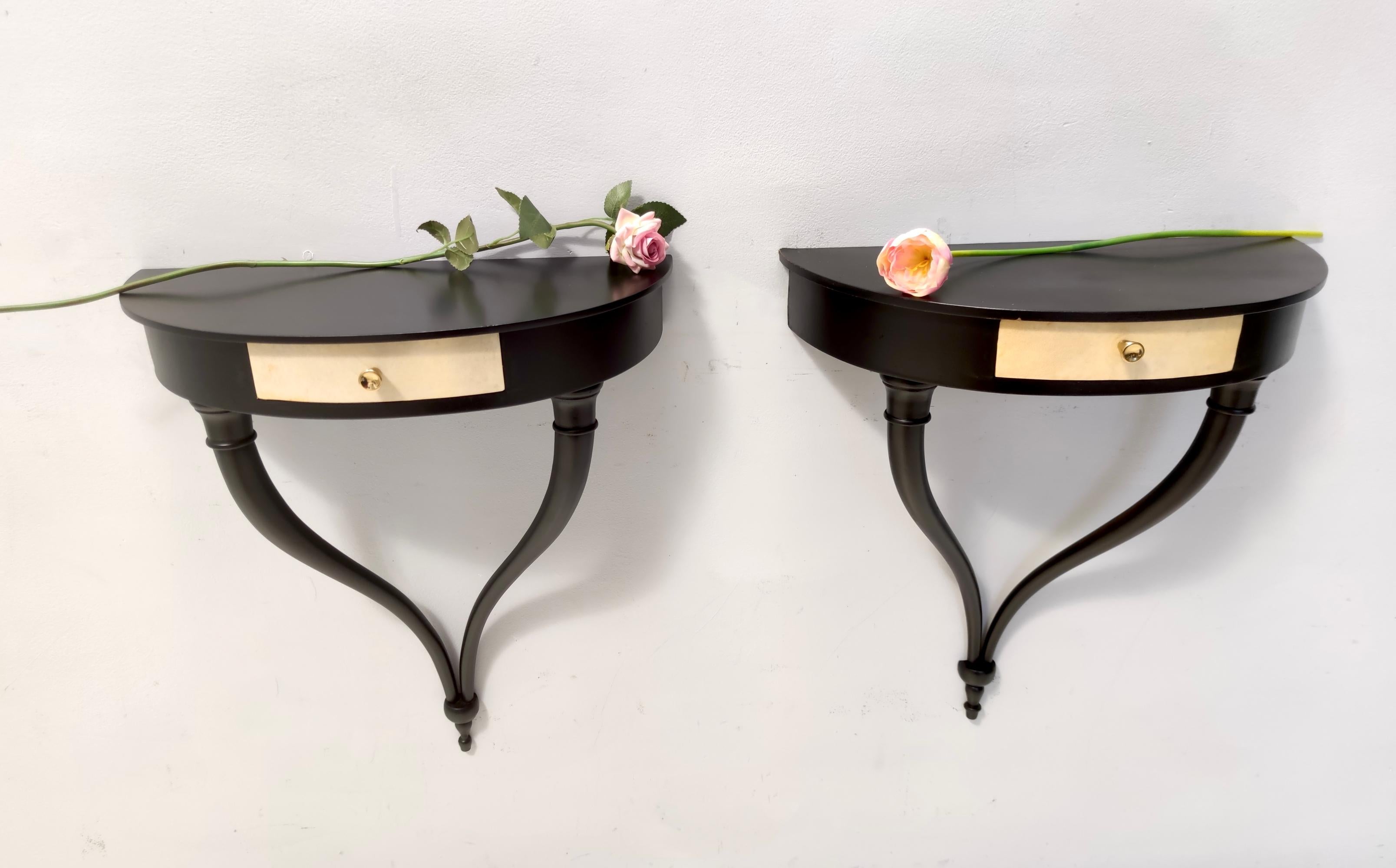 Made in Italy, 1940s.
These wall-mounted console tables / nightstands feature a black ebonized beech frame with brass handles and  parchment drawers.
Ulrich used this sinuous design also for wall lights and sconces. 
They might show slight traces of