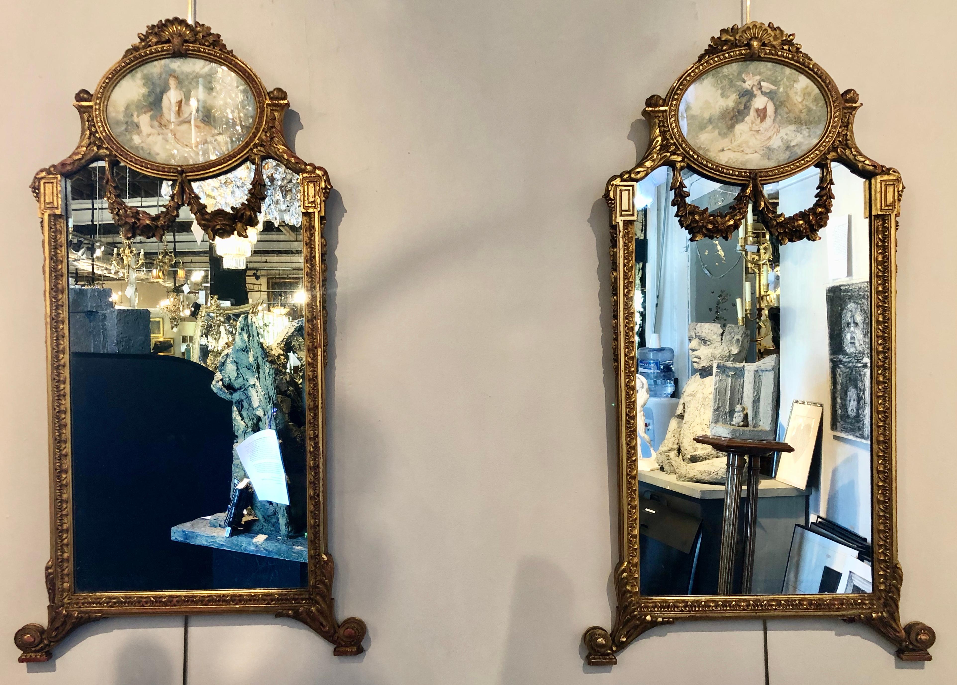 Pair of wall or console mirrors. Finely carved and painted Italian Trumeau mirrors. Each having a painting of a maiden in the woods signed on the lower right in an oval rose carved frame flowing onto a carved rectangular frame. The whole appearing