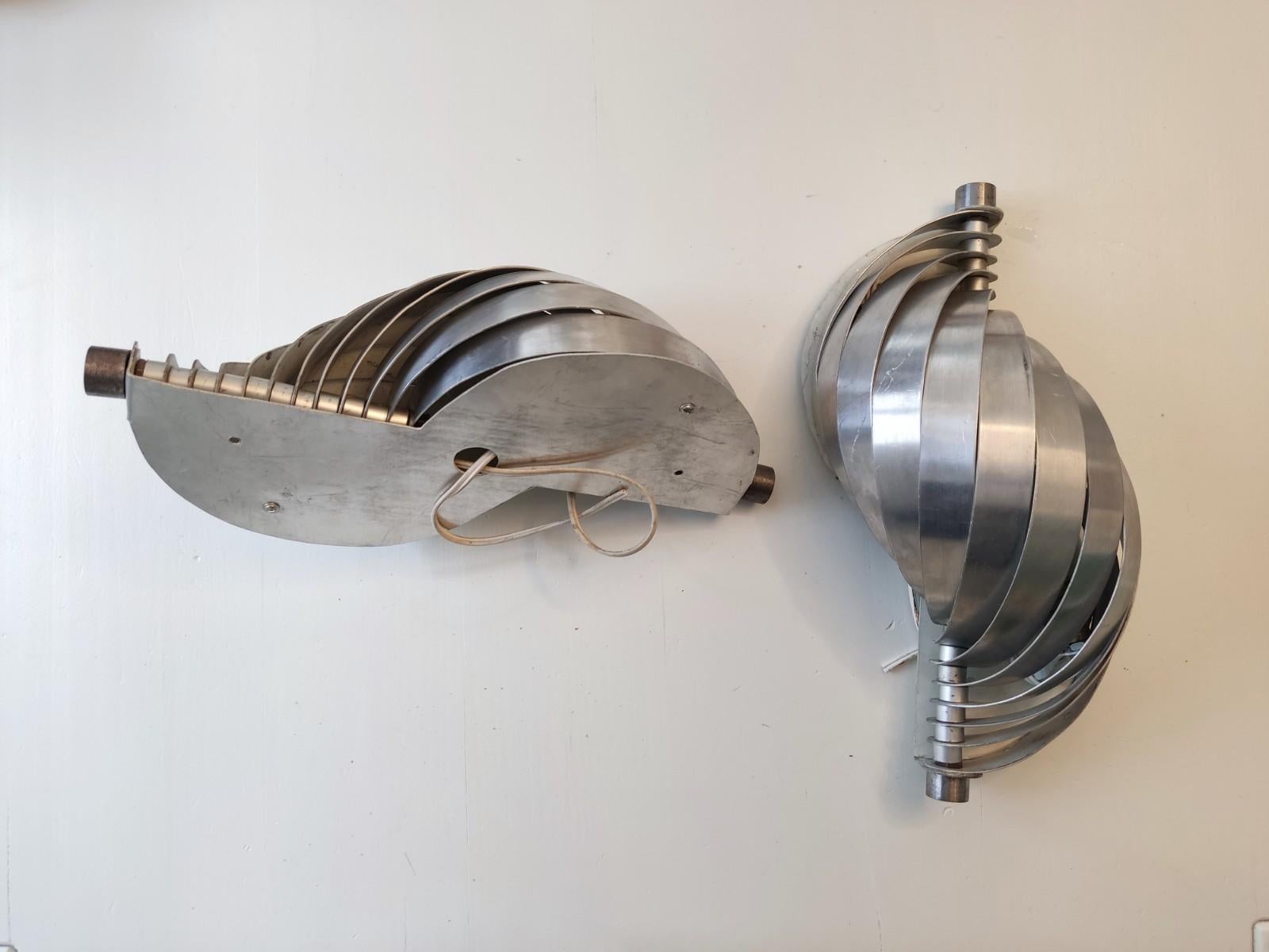 Paire d'appliques attribuées à Henri Mathieu, designer des années 70 connu pour ses lampes faites de lames d'aluminium tendues sur un axe. Une lumière douce et cinétique qui donnera beaucoup d'élégance à votre intérieur. Traces d'utilisation