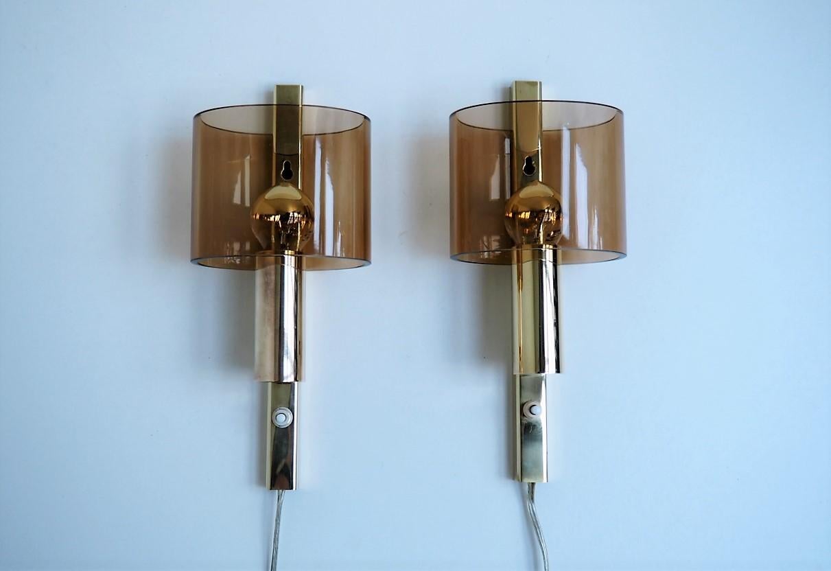 Pair of wall sconces from a danish manufacturer called Hassel & Treud and they are from the 1960´s.

The wall bases are made in solid brass combined with light brown shades made in Plexiglas. They are here showed with two different sets of