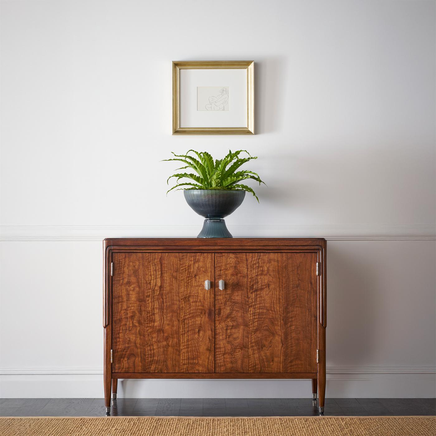 Crafted from exquisite figured walnut, its rich wood grain and slender decorative motif create a statement of understated opulence. The expertly tapered legs and subtle molding details enhance its poised silhouette, while sleek metal hardware adds a