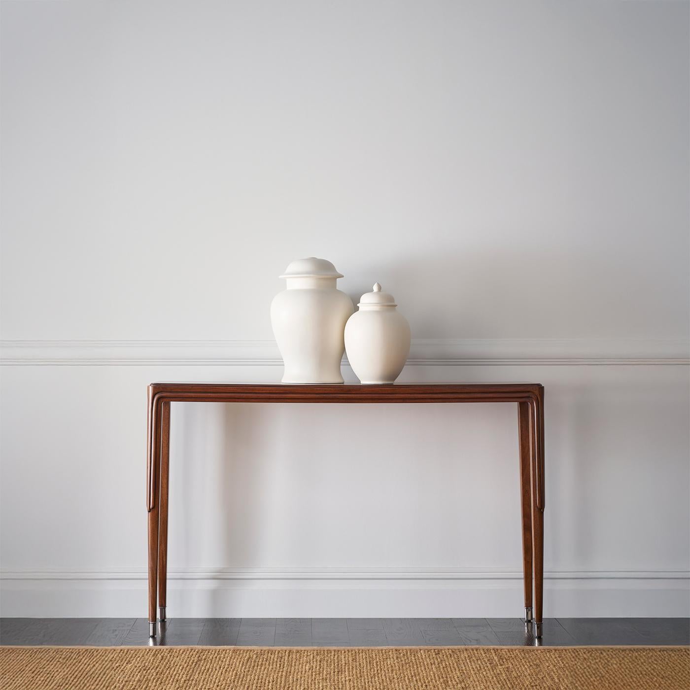 With a slender, decorative motif and a sculptural presence, this piece is a testament to timeless sophistication. The rich figured walnut veneer, finished in a luxurious Mayfair stain, accentuates the natural beauty of the wood grain while enhancing