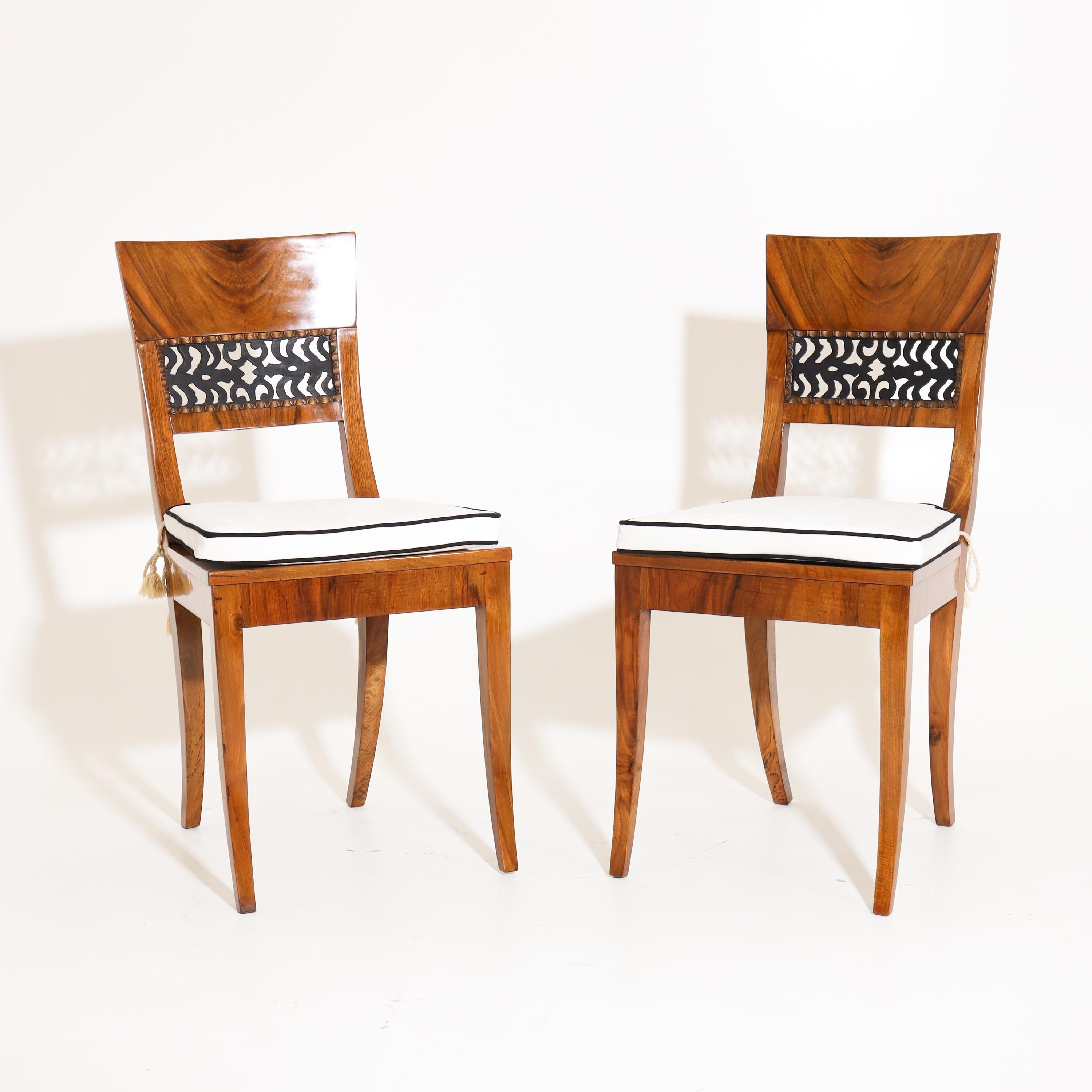 Pair of Biedermeier chairs in walnut veneered, with open-work backrests with wavy, gold-patinated moulding. The seat is covered with Viennese wickerwork. The white seat cushions with black piping are new and are fixed with golden tassels.