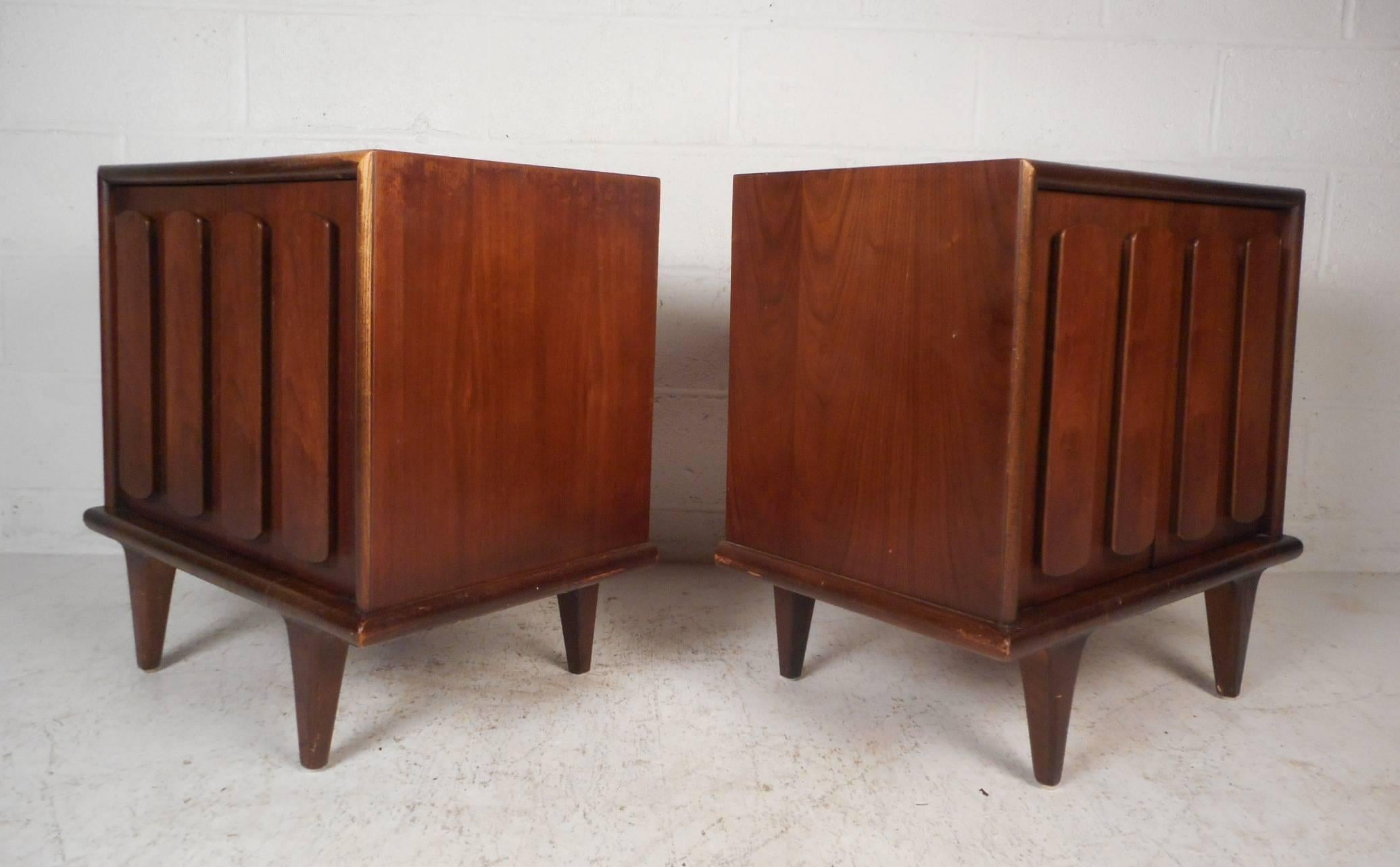 This beautiful pair of Mid-Century Modern nightstands feature two cabinet doors with unusual pulls on the front. The dark walnut finish and tapered legs show quality craftsmanship. These stylish vintage modern case pieces have plenty of room for