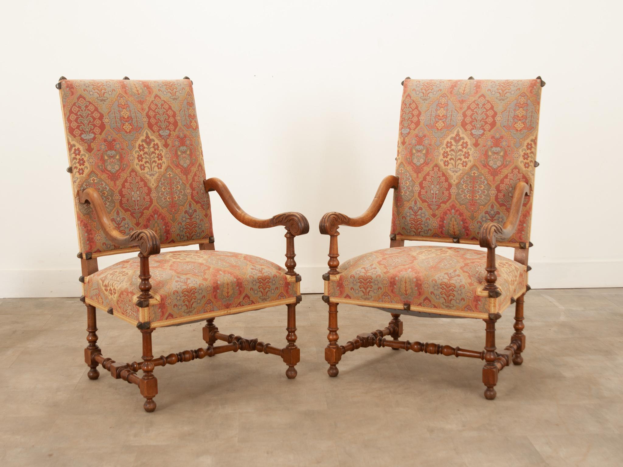 A wonderful pair of French 19th Century walnut Os de Mouton armchairs. These large armchairs are upholstered in a printed tapestry fabric, trimmed in tape and affixed with oversized brass nailheads. The curved Os de Mouton “mutton bone” arms not