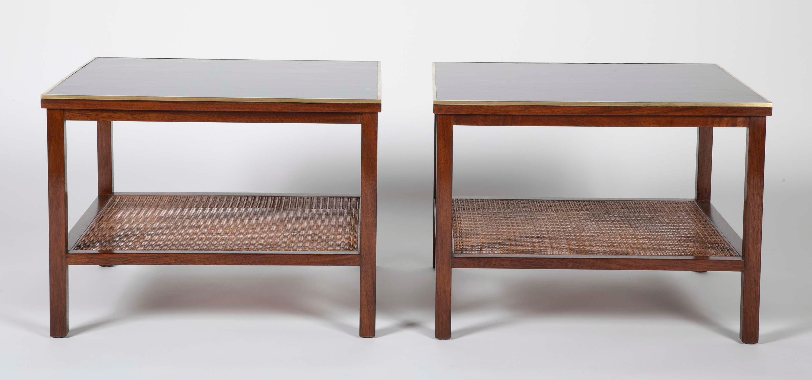 A pair of Paul McCobb Side tables in Walnut with caned shelves. The tops are black leather bound inside a brass boarder. Both tables retain their Paul McCobb design for Calvin Furniture labels.