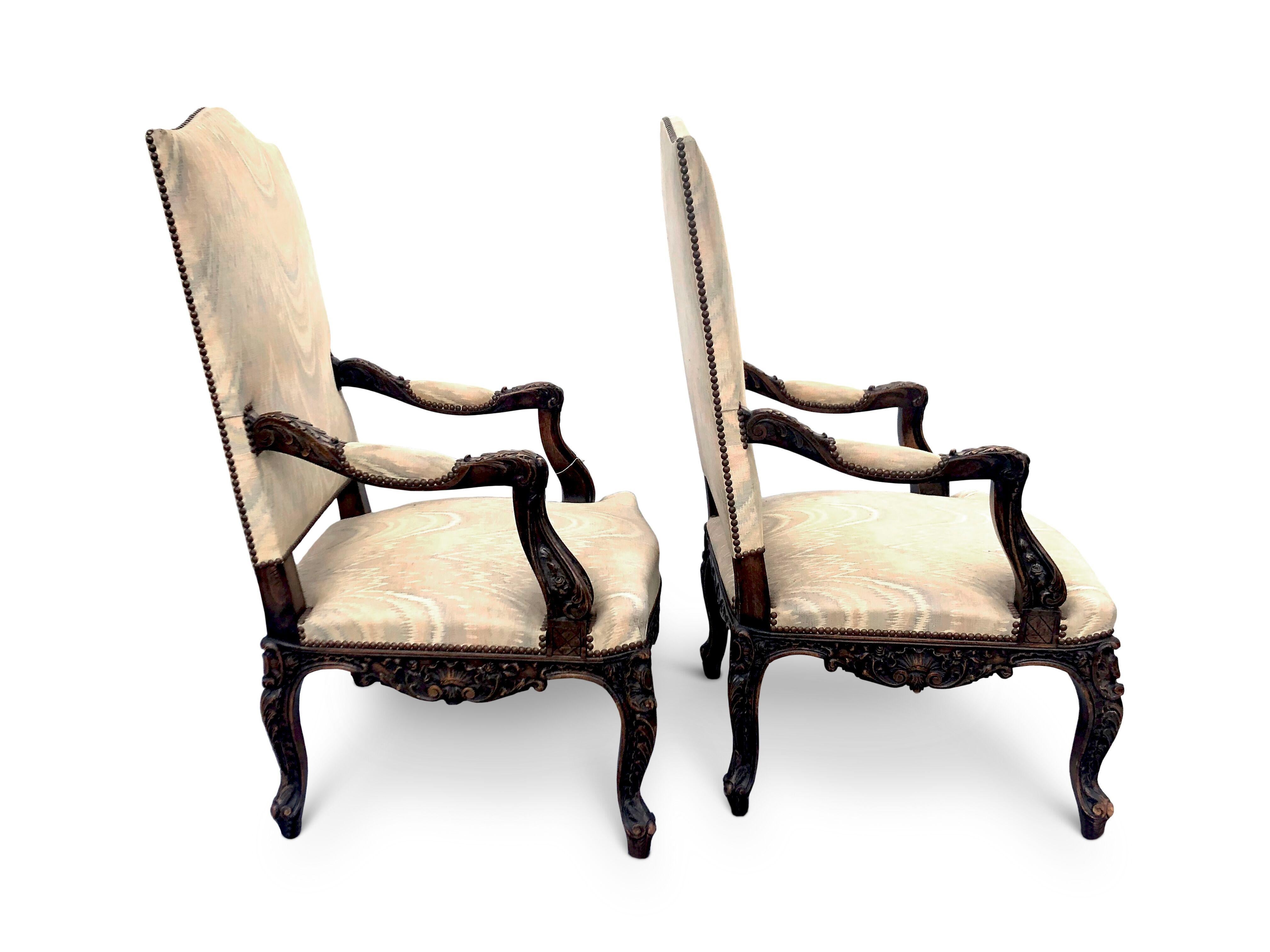 Pair of early 20th century upholstered Gainsborough armchairs.
High camel backs, semi upholstered arms, the seat above acanthus/foliage carving to the frieze, sides and cabriole legs.