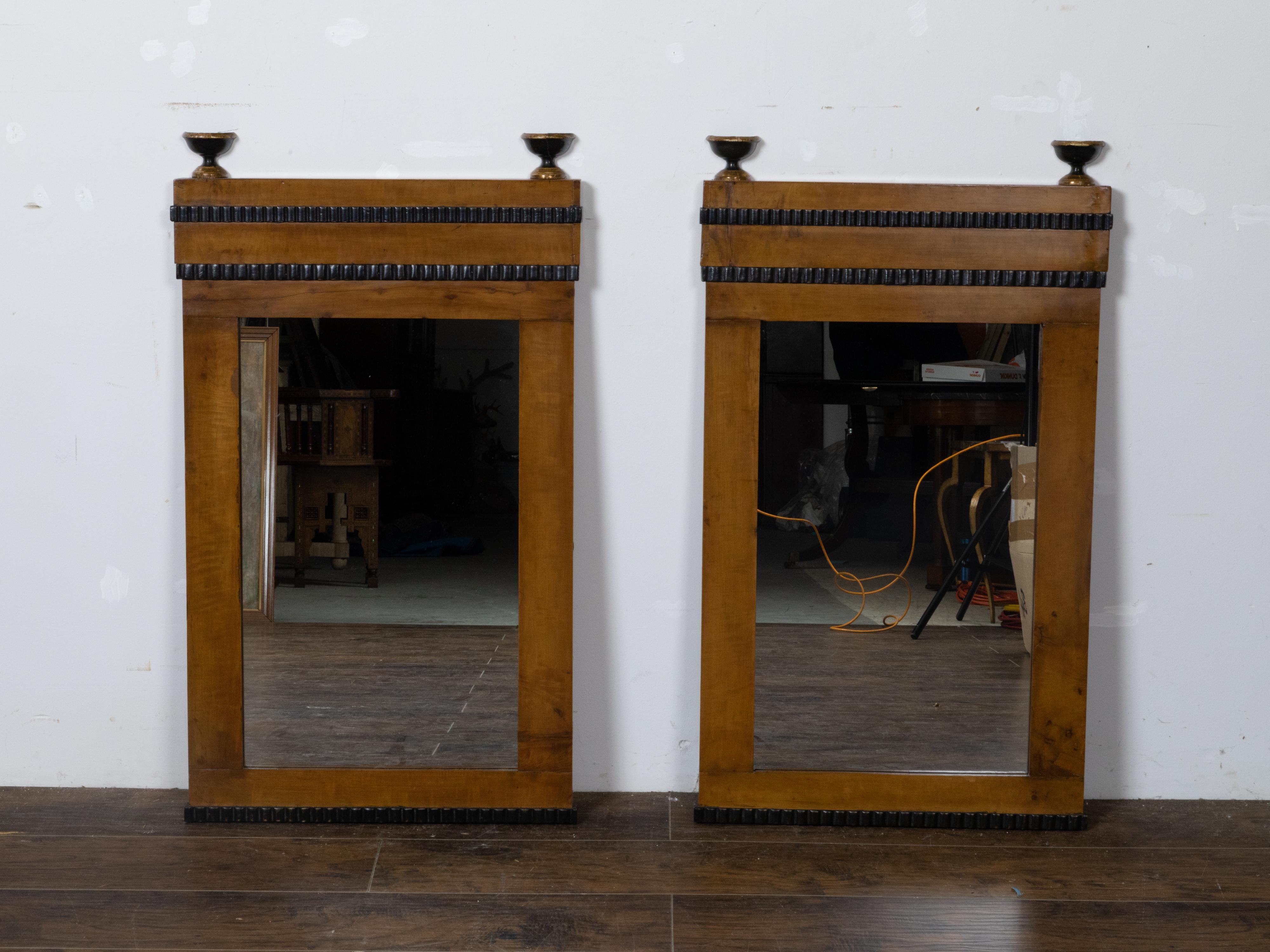 A small pair of Austrian walnut mirrors from the 19th century made of old Biedermeier components, with dark brown color, ebonized reeded motifs and turned finials with gilt accents. Immerse yourself in Austrian craftsmanship with this pair of modern