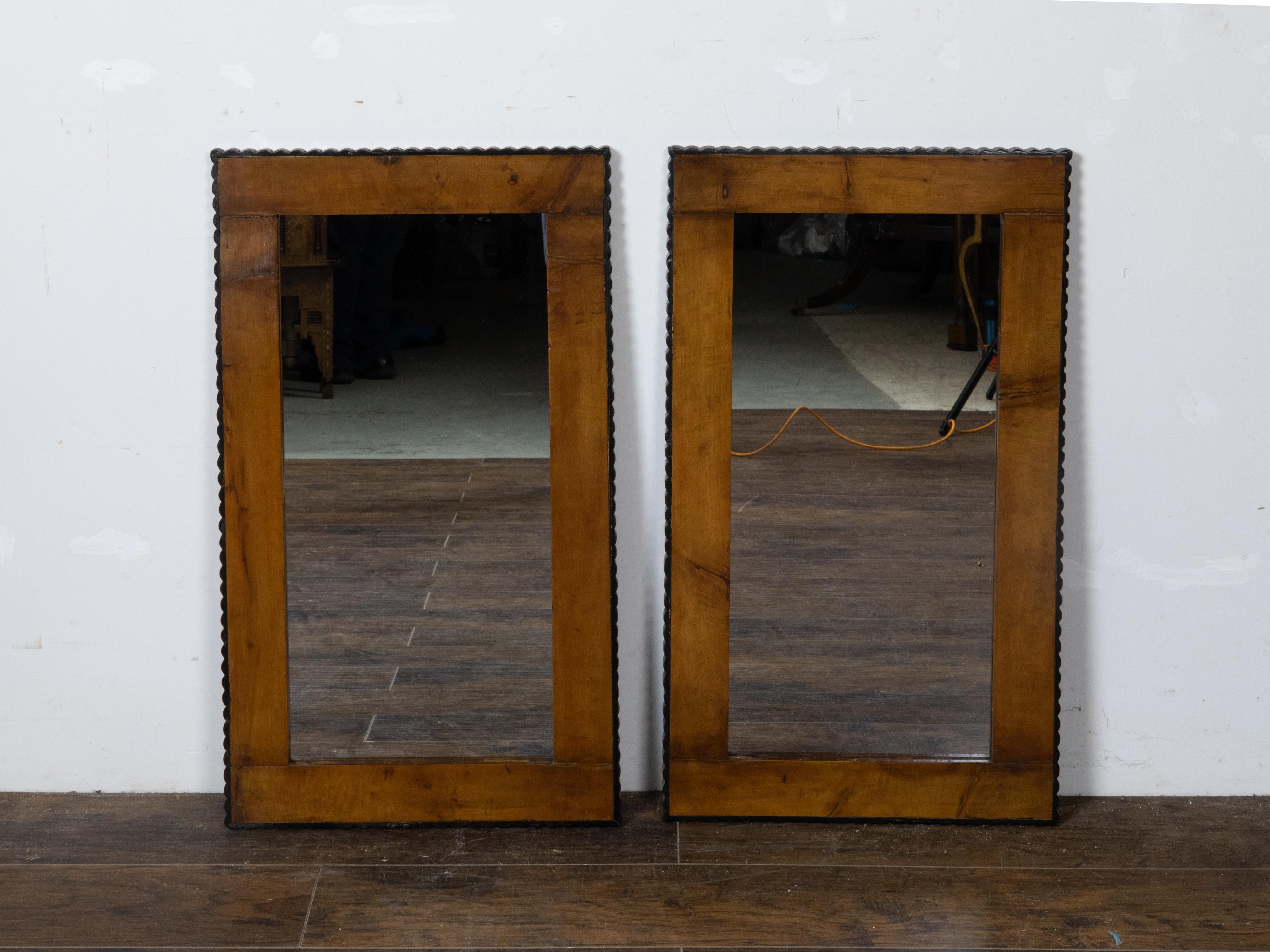 A pair of walnut mirrors from the 19th century made of old Biedermeier components, with dark brown color and ebonized scalloped edges. This pair of walnut mirrors from the 19th century, was expertly crafted using old Biedermeier components. The