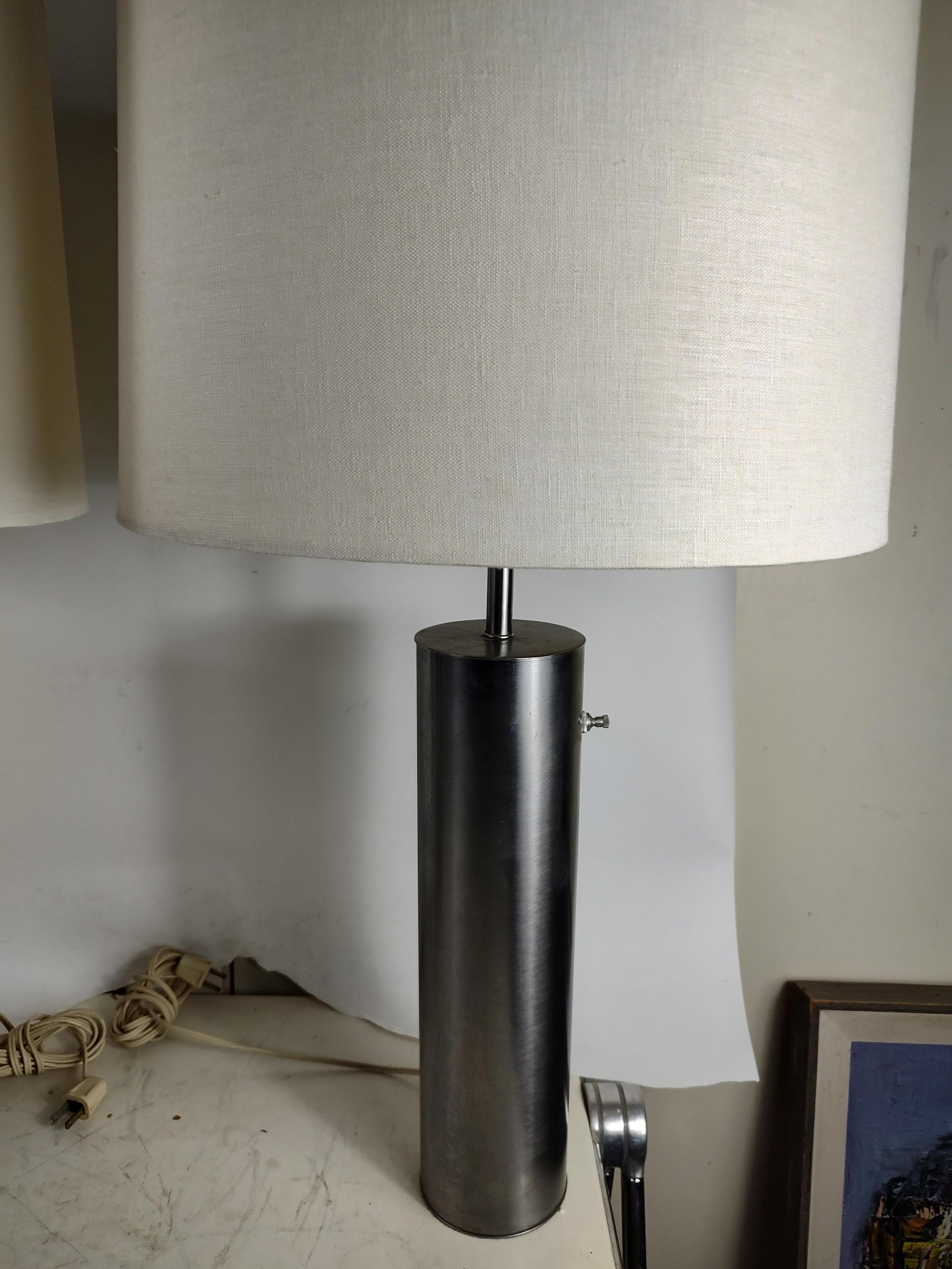 Fabulous pair of stainless cylindrical table lamps by the Nessen lighting Co. In excellent vintage condition with minimal wear, no scratches or dings to the metal. Sold as a pair. Shades not included. Shades pictured are 15x 11. Lamps are 28.75 to