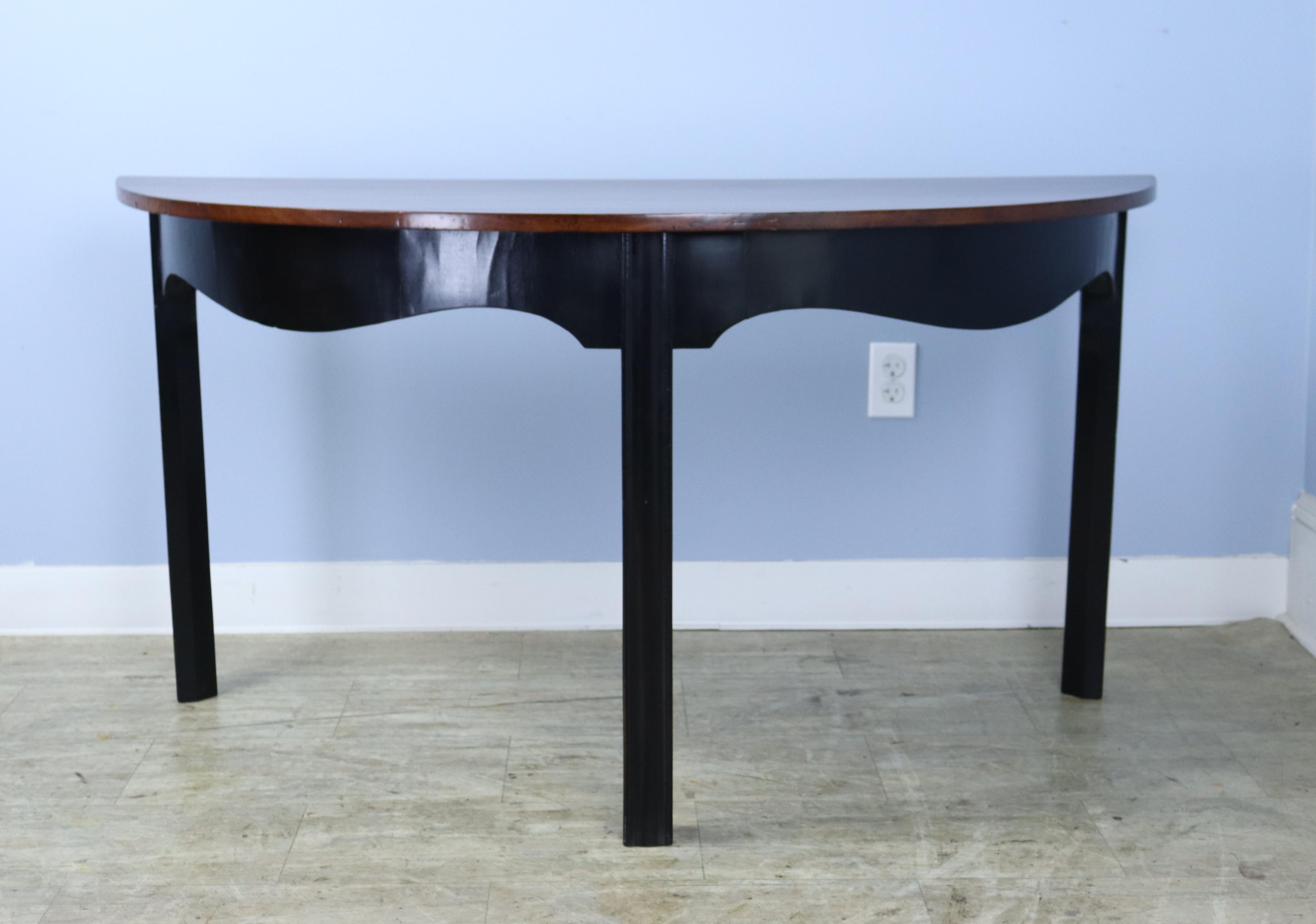 A pair of large walnut demi-lune console tables with ebonized bases.  Would look smart on either side of an archway or window.  Note that when put together, they do not form a perfect circle.  There are some light scratches and a small chip in one