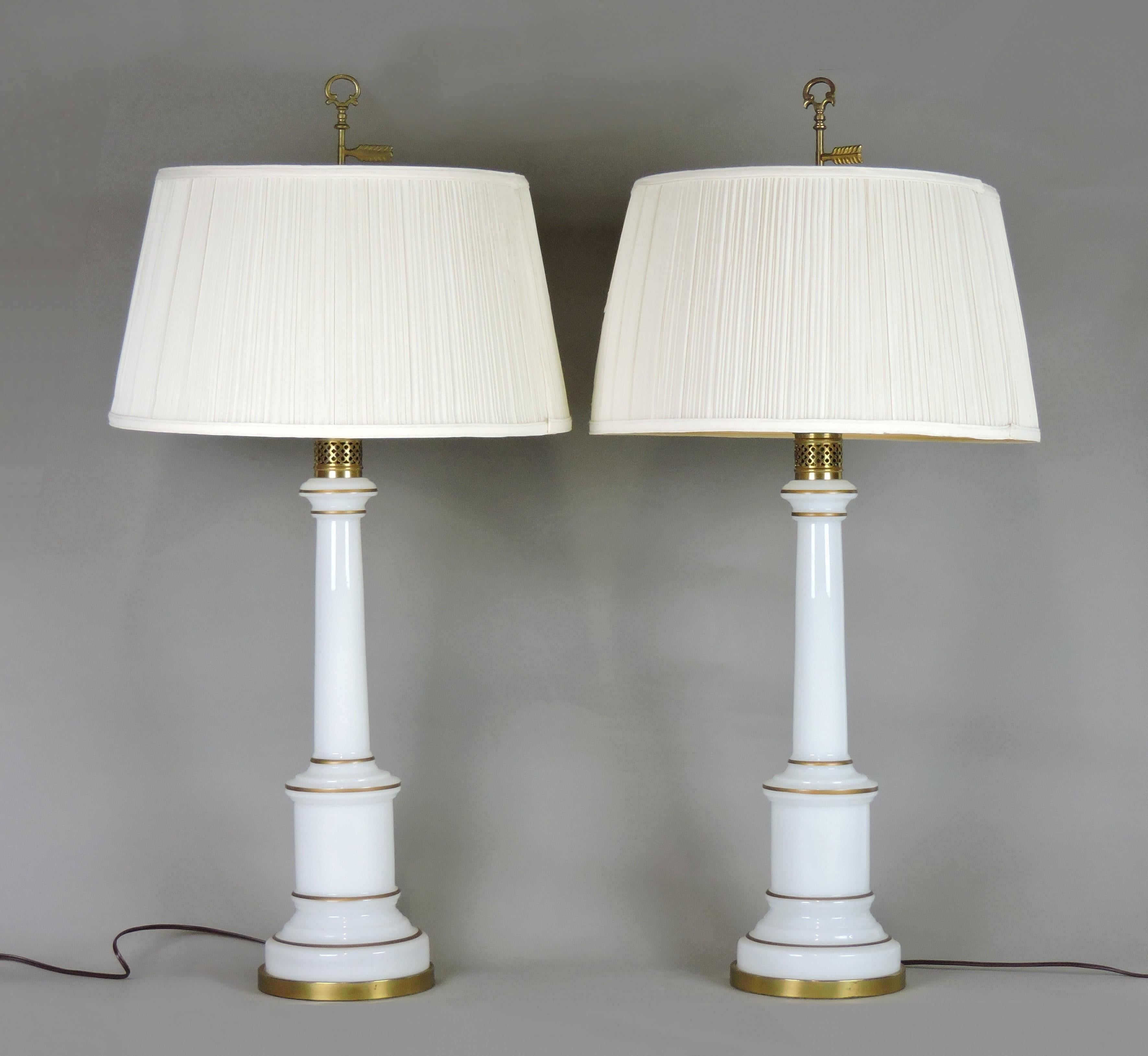 Elegant pair of table lamps by high end lamp manufactuer, Warren Kessler of New York. These lamps are made of white opaline glass with gilt pinstriping and brass accents. These have all new wiring and each take a standard base three-way bulb. The