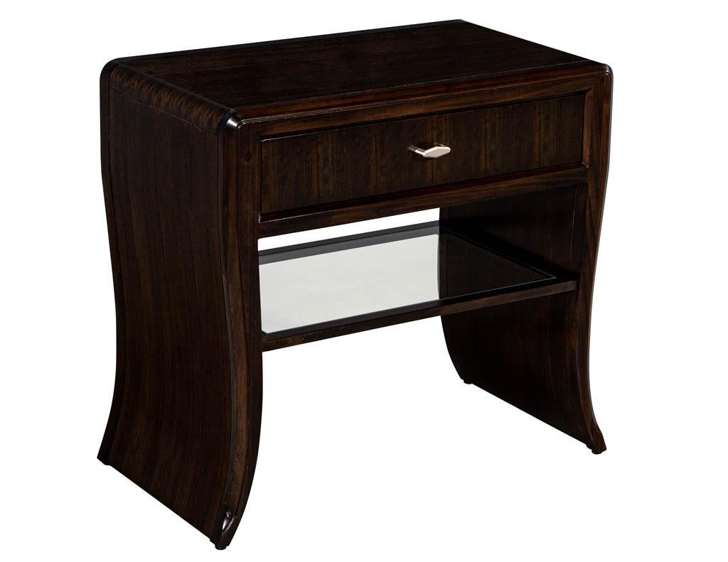Pair of Waterfall Mozambique and Mahogany end tables. Beautiful sculpted waterfall design with large storage drawer and open glass shelf compartment. Featuring metal knobs and unique Mozambique wood grains. Finished in a dark espresso with a slight