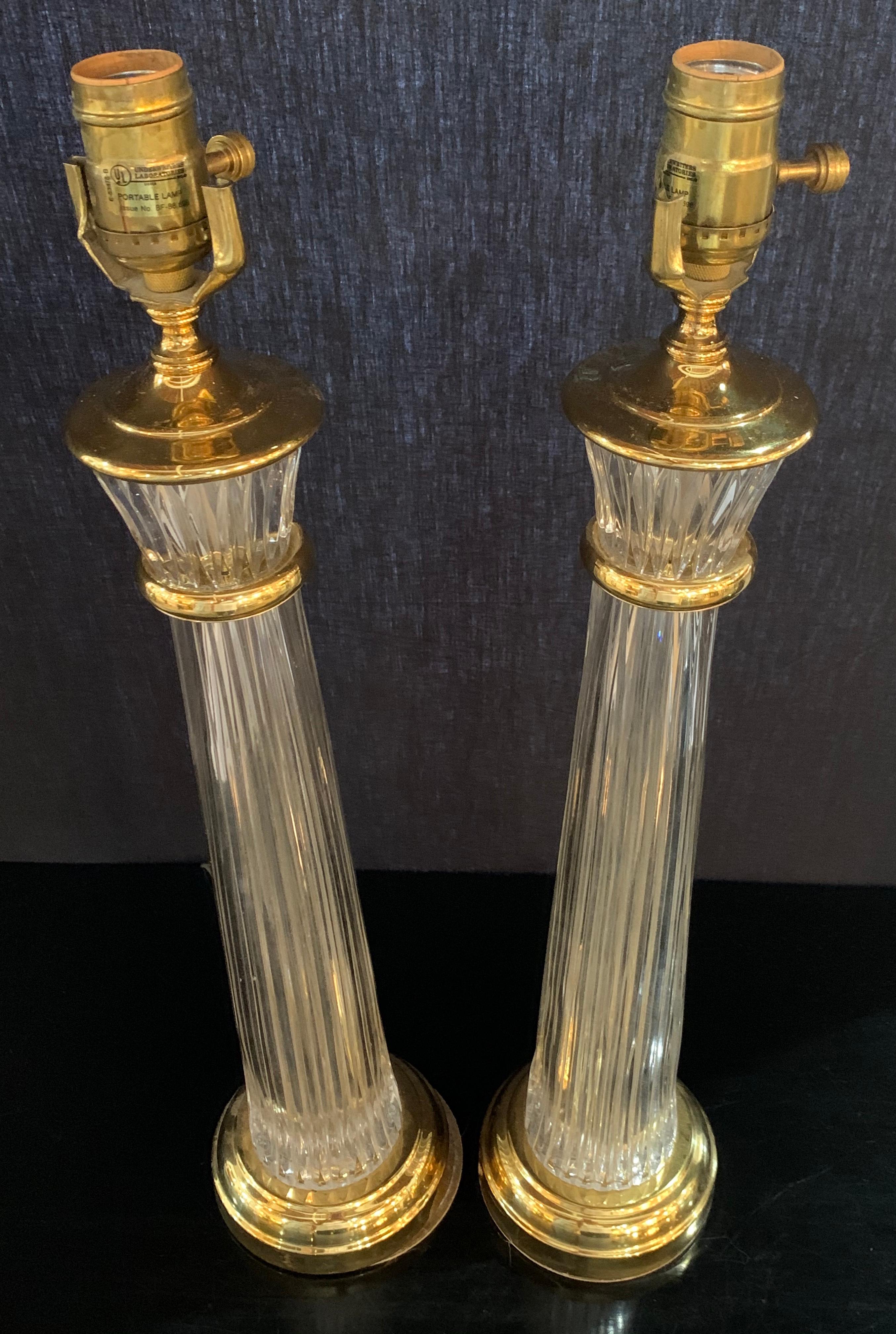Pair of Waterford Hollywood Regency style column form table lamps in the neoclassical manner. Each of these sleek and lean table lamps have brass framed crystal bases and upper framed crystal cups leading to a single light. The bases each acid