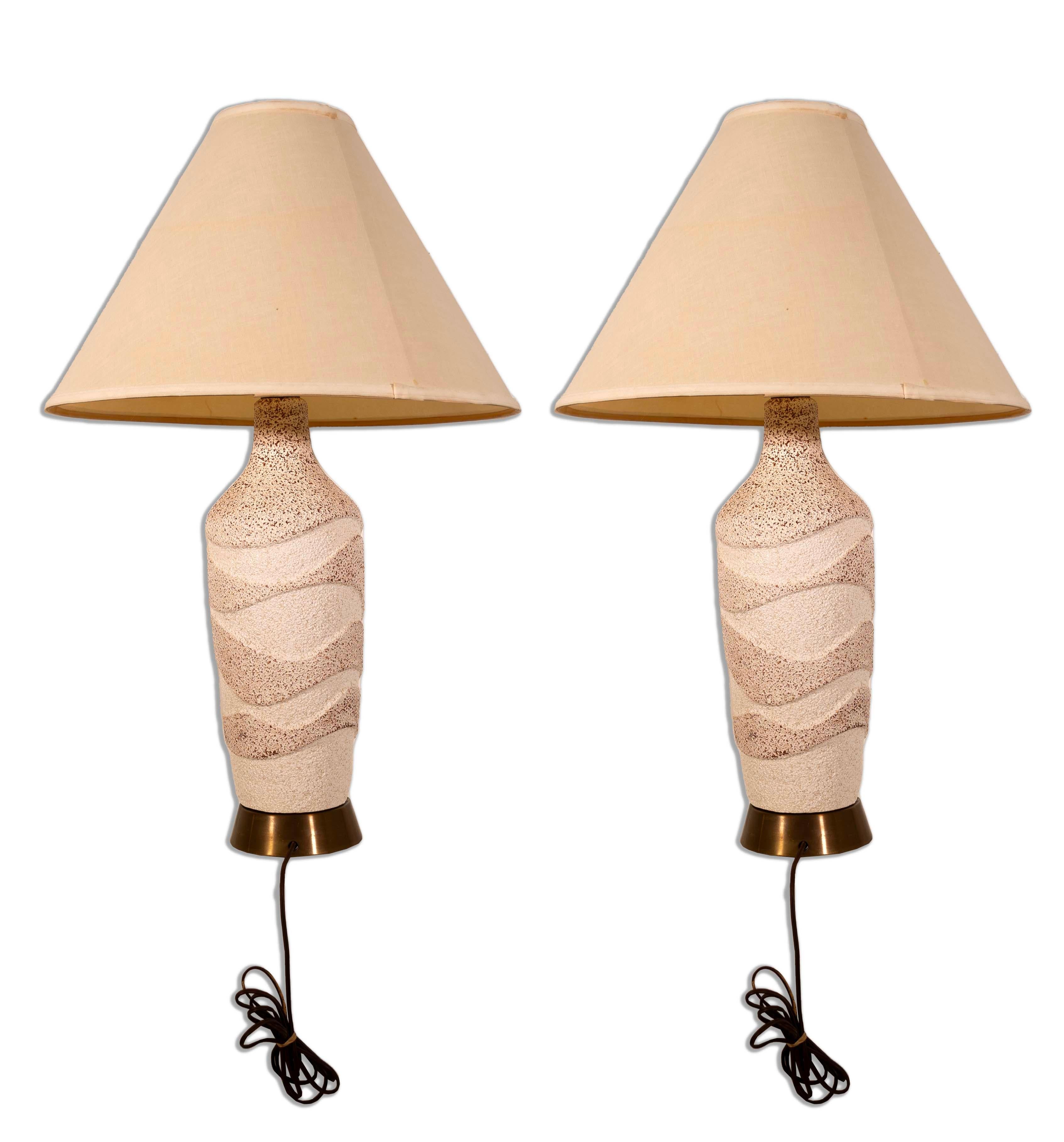 Chaleureuse et accueillante, cette paire de lampes en céramique texturée ondulée est la quintessence du charme moderne du milieu du siècle dernier. Le design ondulé unique de la base en céramique, associé à la douce lueur des abat-jour beiges, crée