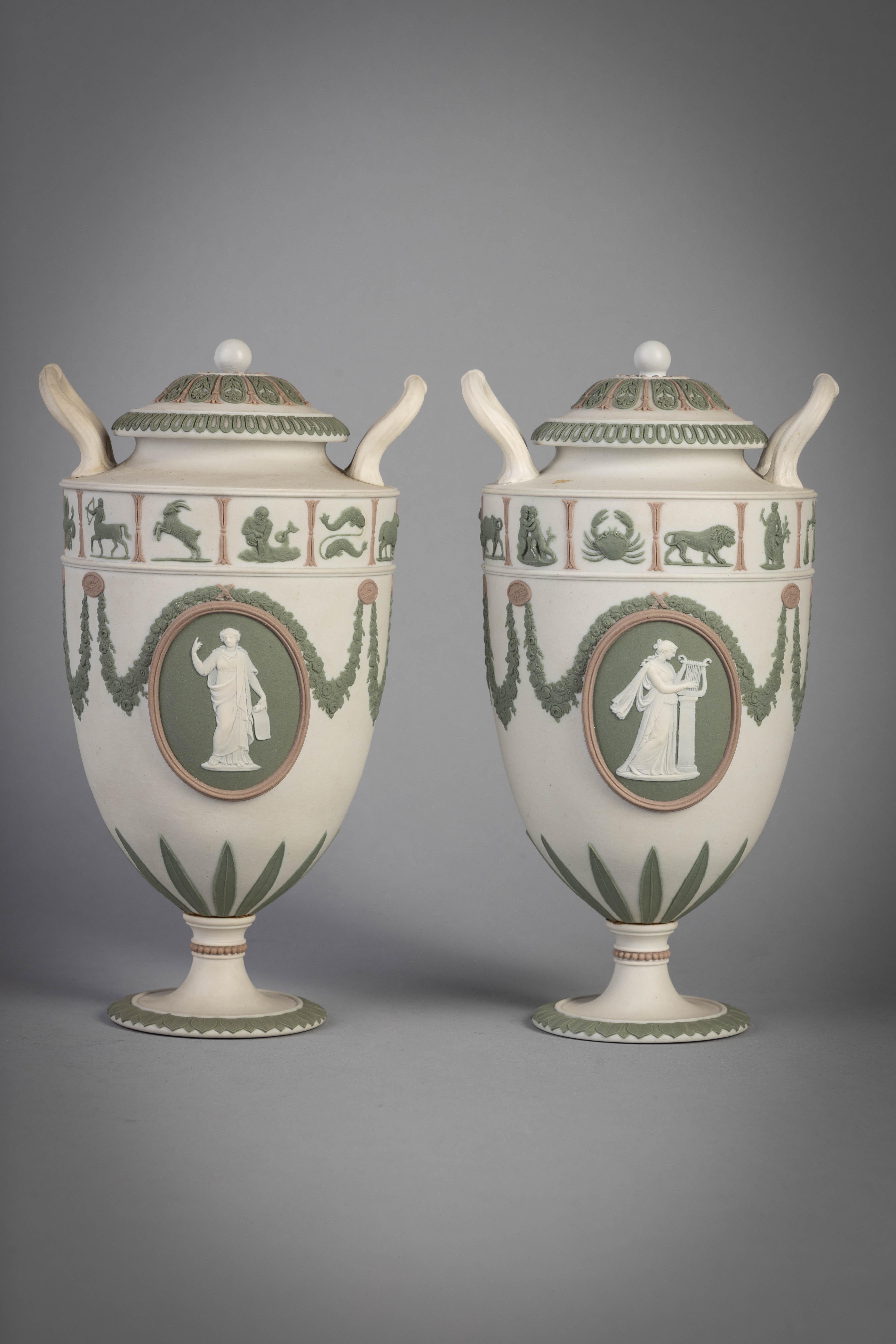 Sage green and lilac jasperware. Each sharply shouldered two-handled ovoid urn decorated with oval figural medallions beneath floral swags and band of Zodiac symbols, the cover with ball final on circular foot, impressed WEDGWOOD.